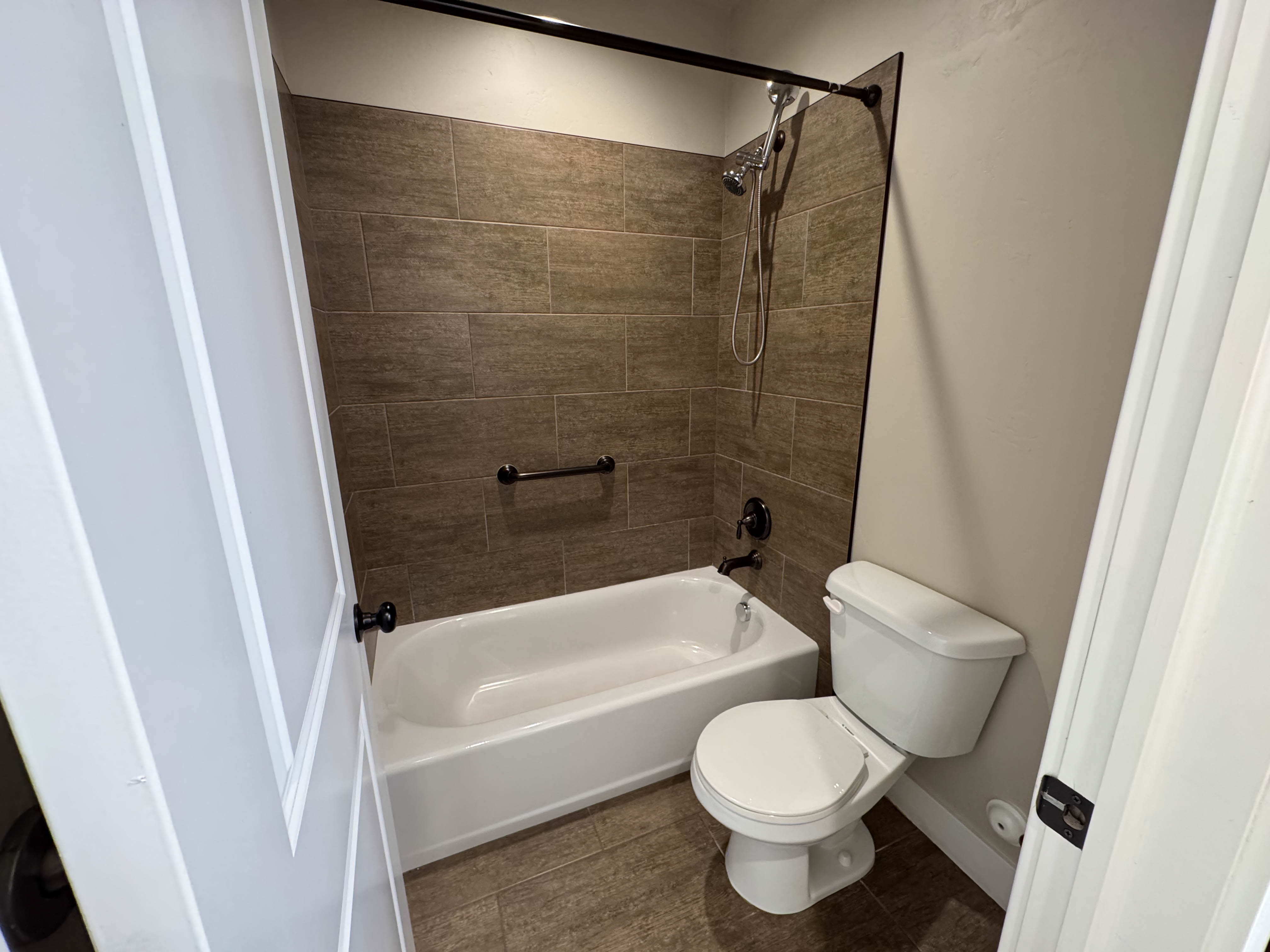 Full bathroom featuring a tub/shower combination with brown subway tile surround, matte black fixtures, and a coordinating grab bar