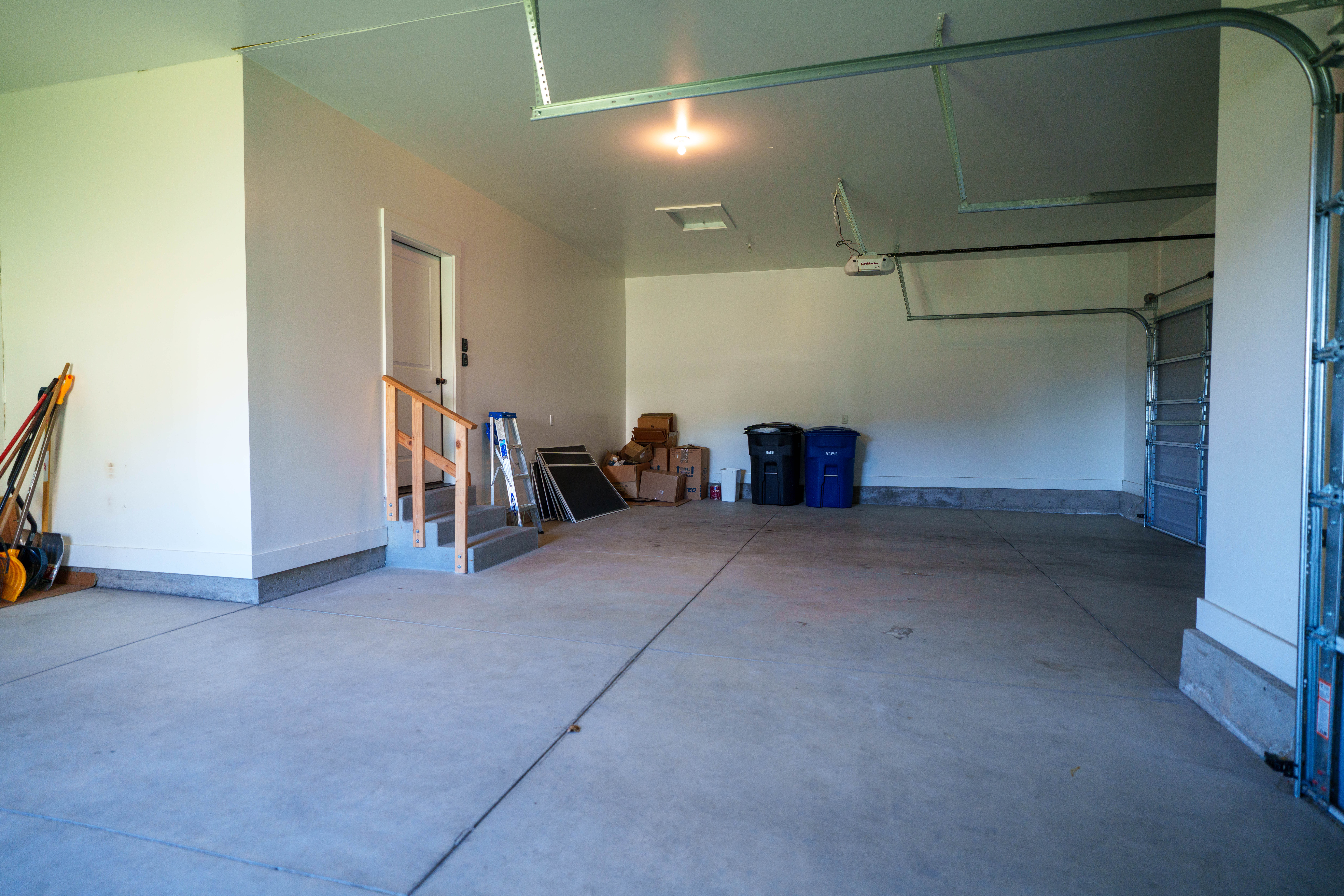 Spacious three-car garage with a concrete floor, bright overhead lighting, direct interior access, and an automatic garage door opener