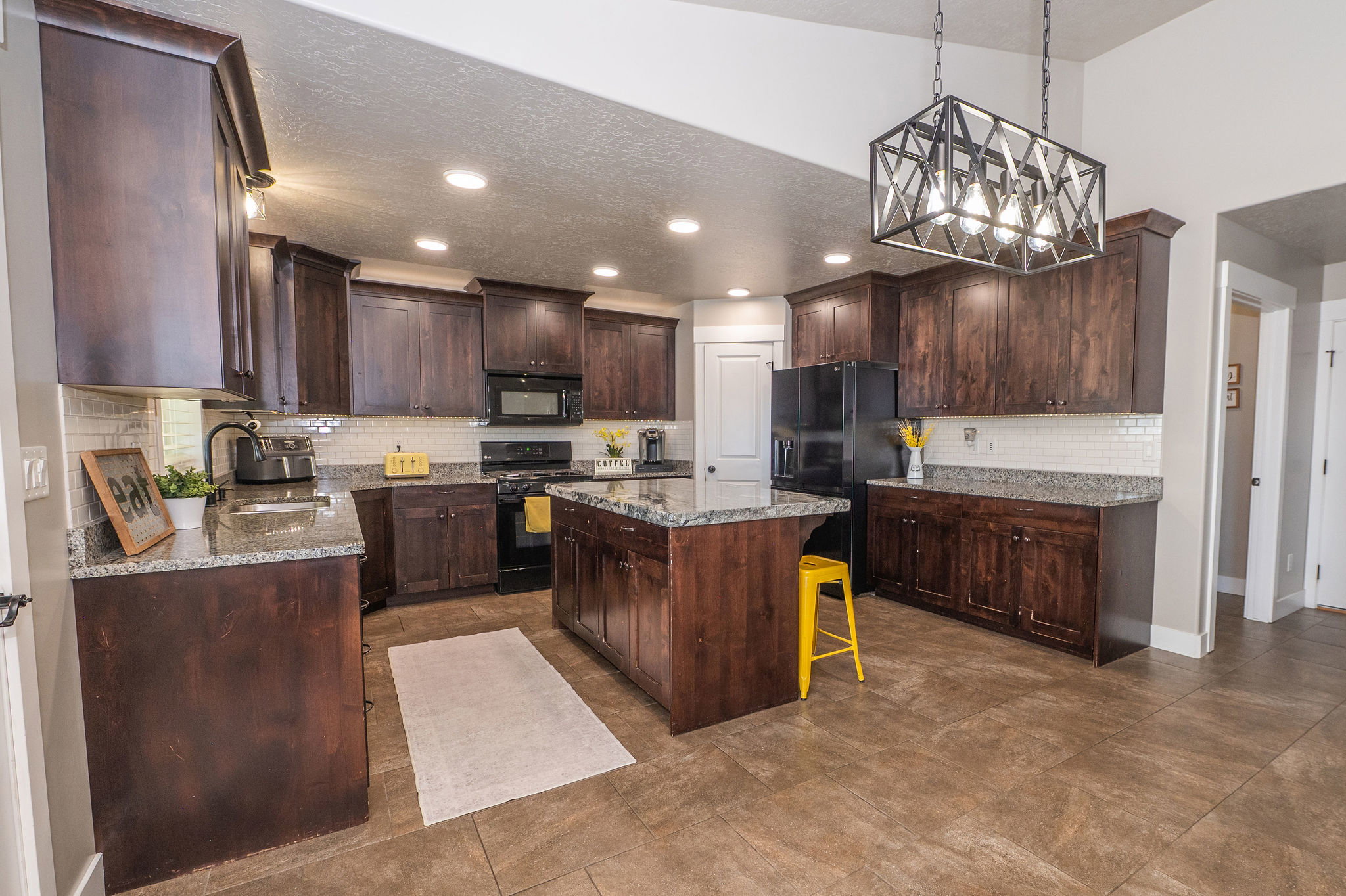 Spacious kitchen featuring dark wood cabinetry, light granite countertops, a central island with bar seating, tiled flooring, and recessed lighting