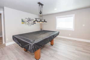 Spacious recreation area featuring light wood-finish flooring, a contemporary industrial-style light fixture, and a window with blinds