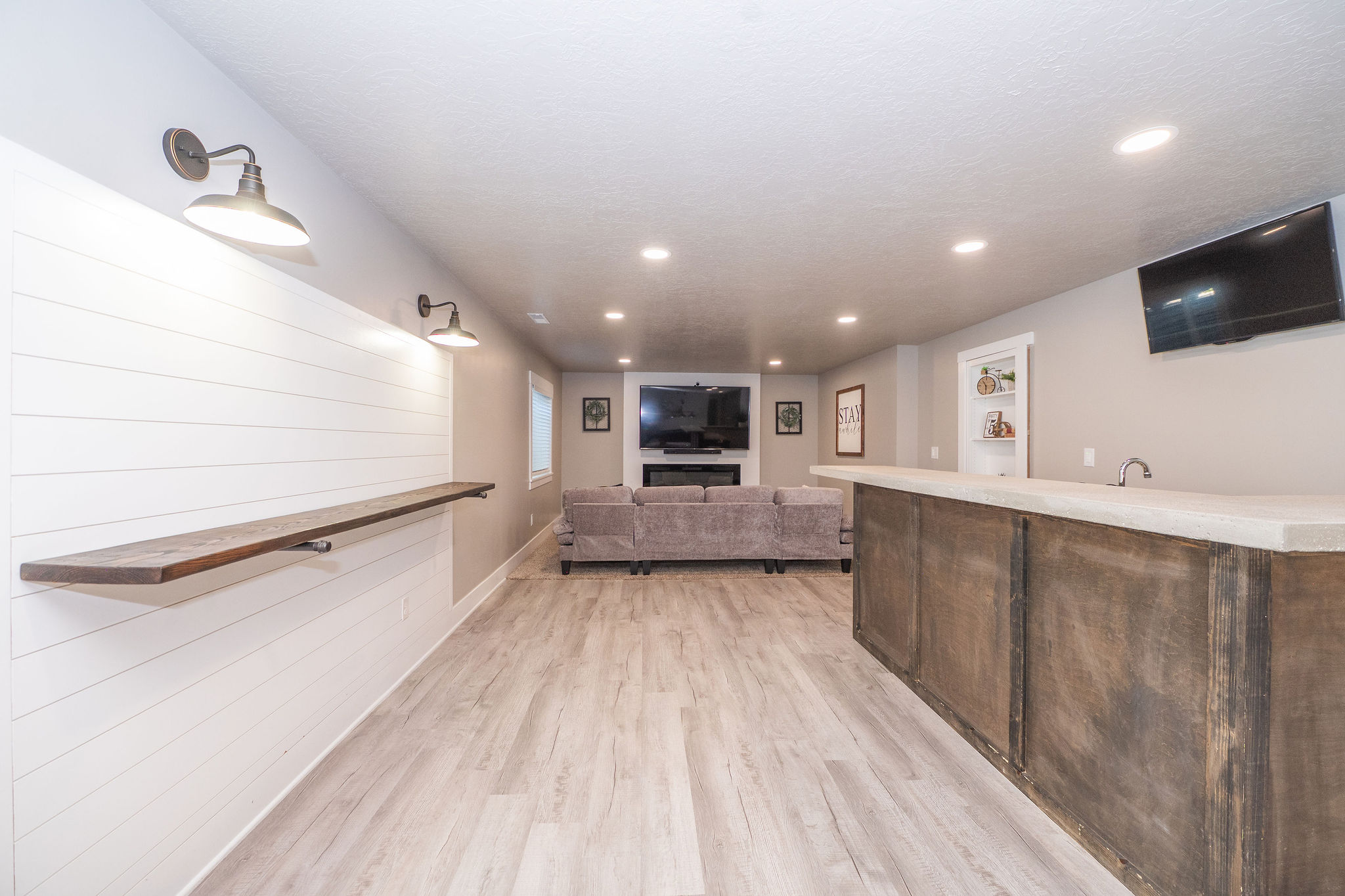 Open-concept lower level featuring shiplap accent wall with sconce lighting, wood-finish flooring, a built-in wet bar with sink, and recessed lighting