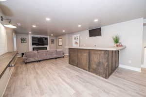 Expansive entertainment space featuring a custom bar with a light-toned countertop, a built-in electric fireplace with a white mantel, recessed lighting, and wood-finish flooring