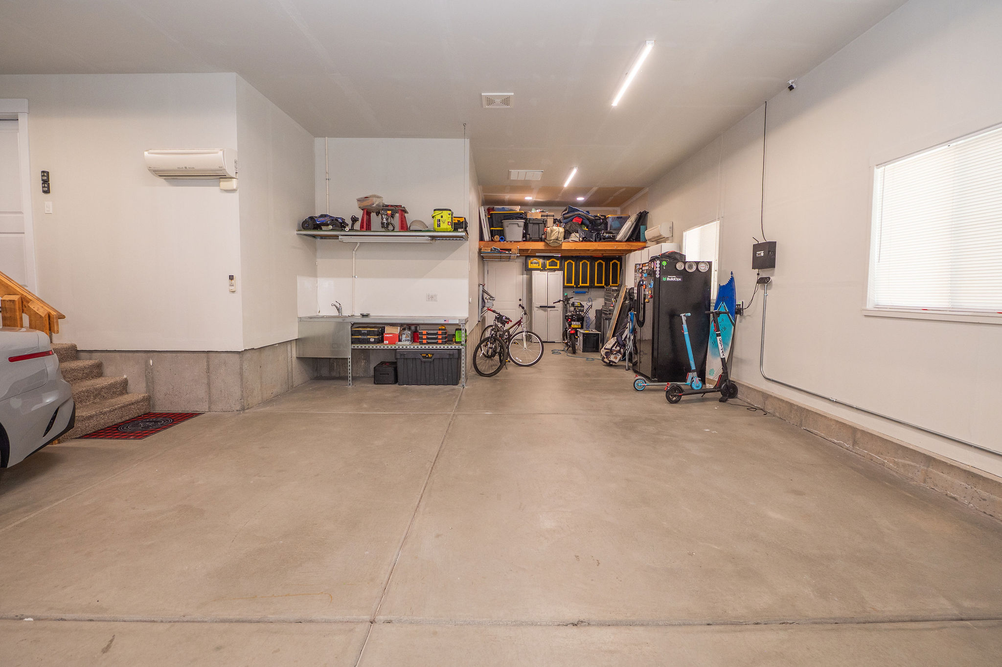 Spacious garage with concrete flooring, built-in shelving, a utility sink, and wall-mounted lighting
