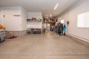 Spacious garage with concrete flooring, built-in shelving, a utility sink, and wall-mounted lighting
