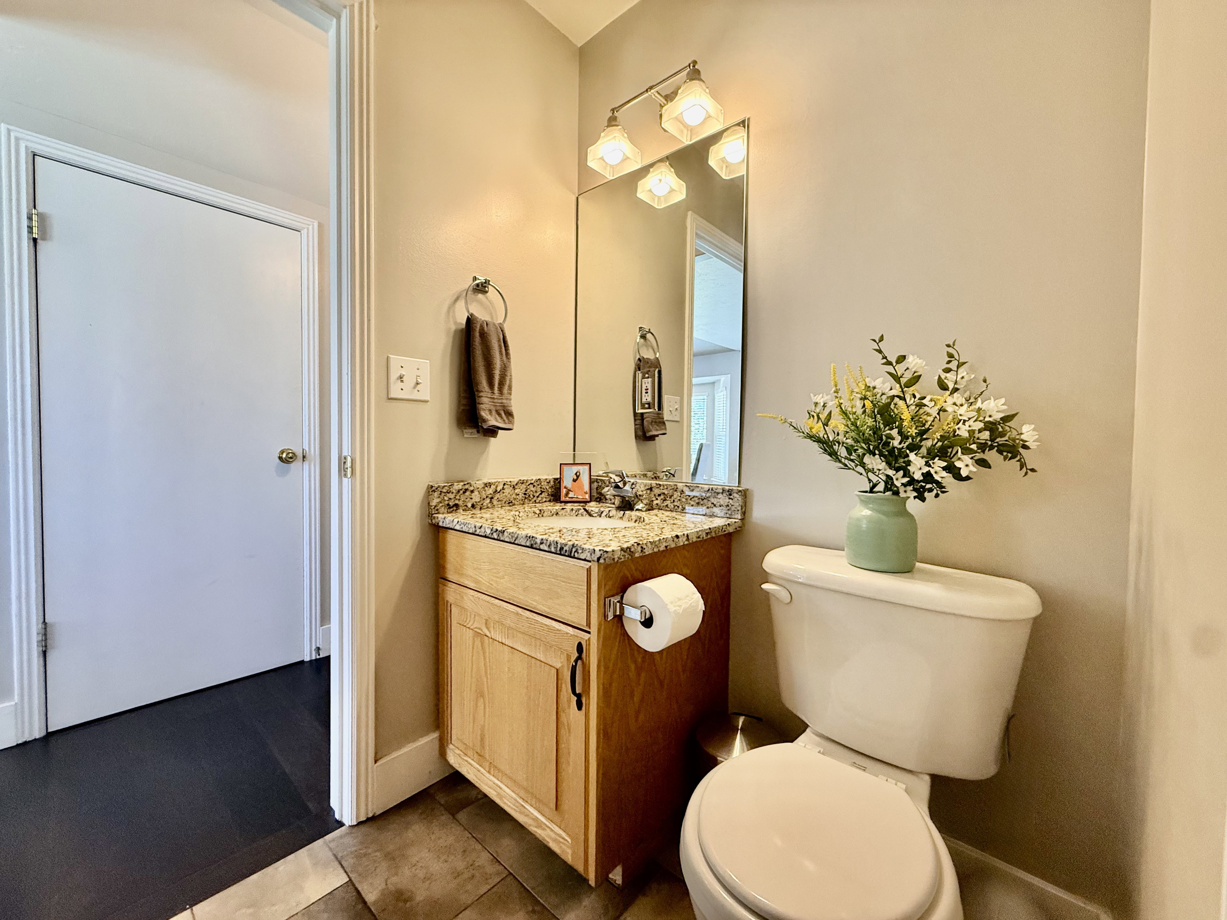 Powder room featuring a light wood-finish vanity with a granite countertop, undermount sink, and a framed mirror with overhead lighting