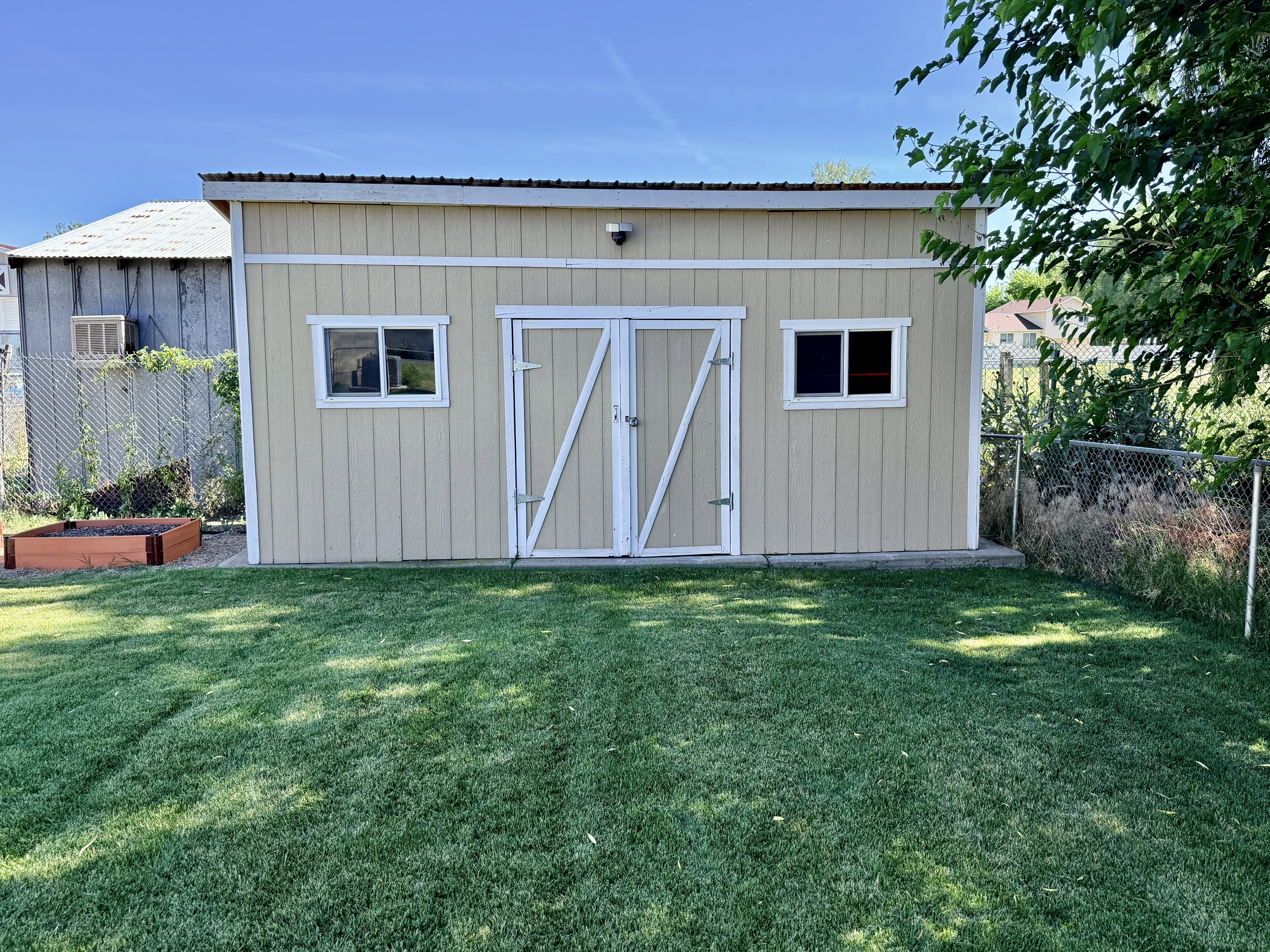 Exterior storage shed with a metal roof, two windows, double barn-style doors, and a neutral-toned siding finish
