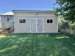 Exterior storage shed with a metal roof, two windows, double barn-style doors, and a neutral-toned siding finish