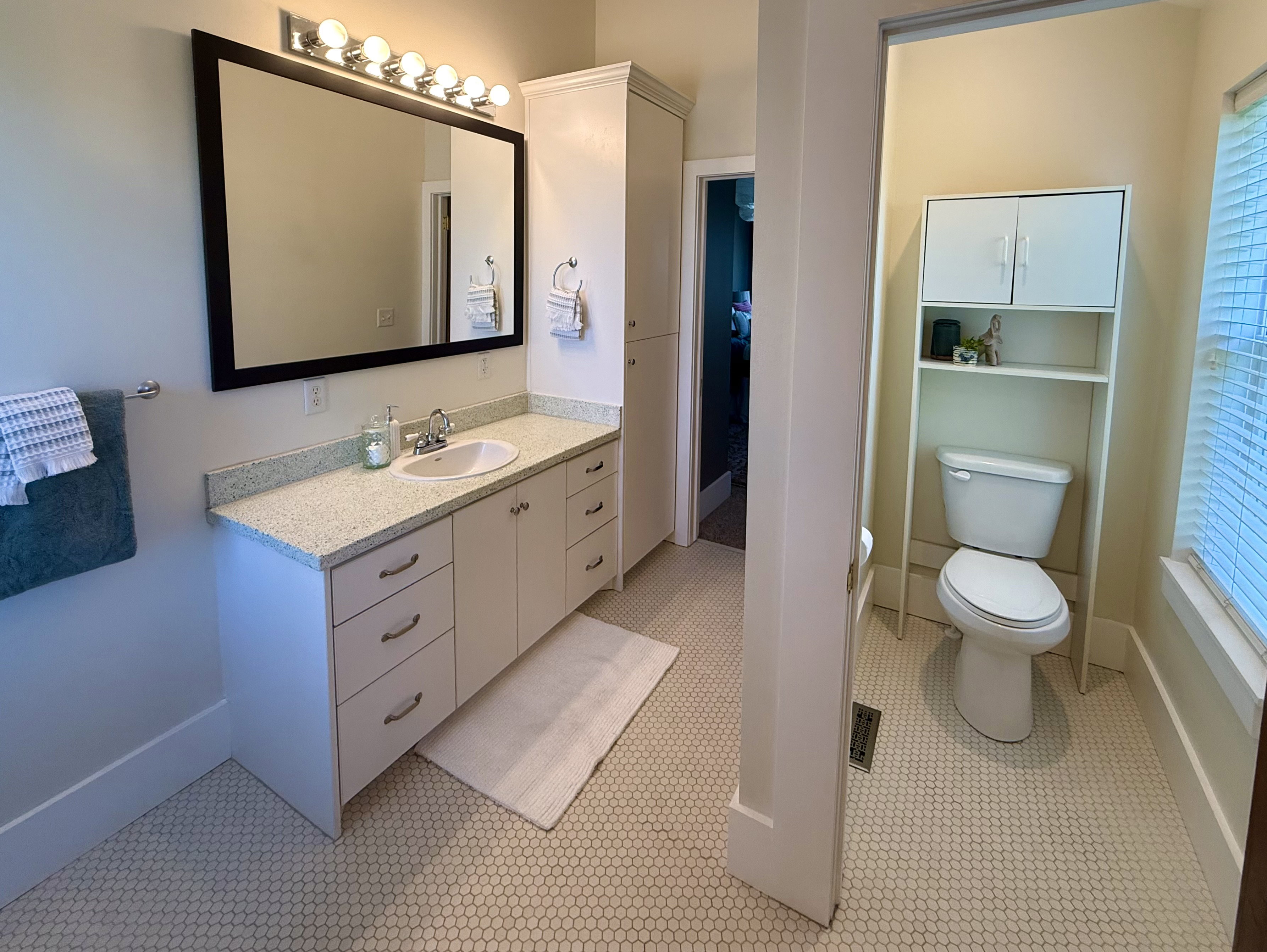 Bathroom featuring a white vanity with an undermount sink, a countertop with light flecking, and a large framed mirror with overhead lighting