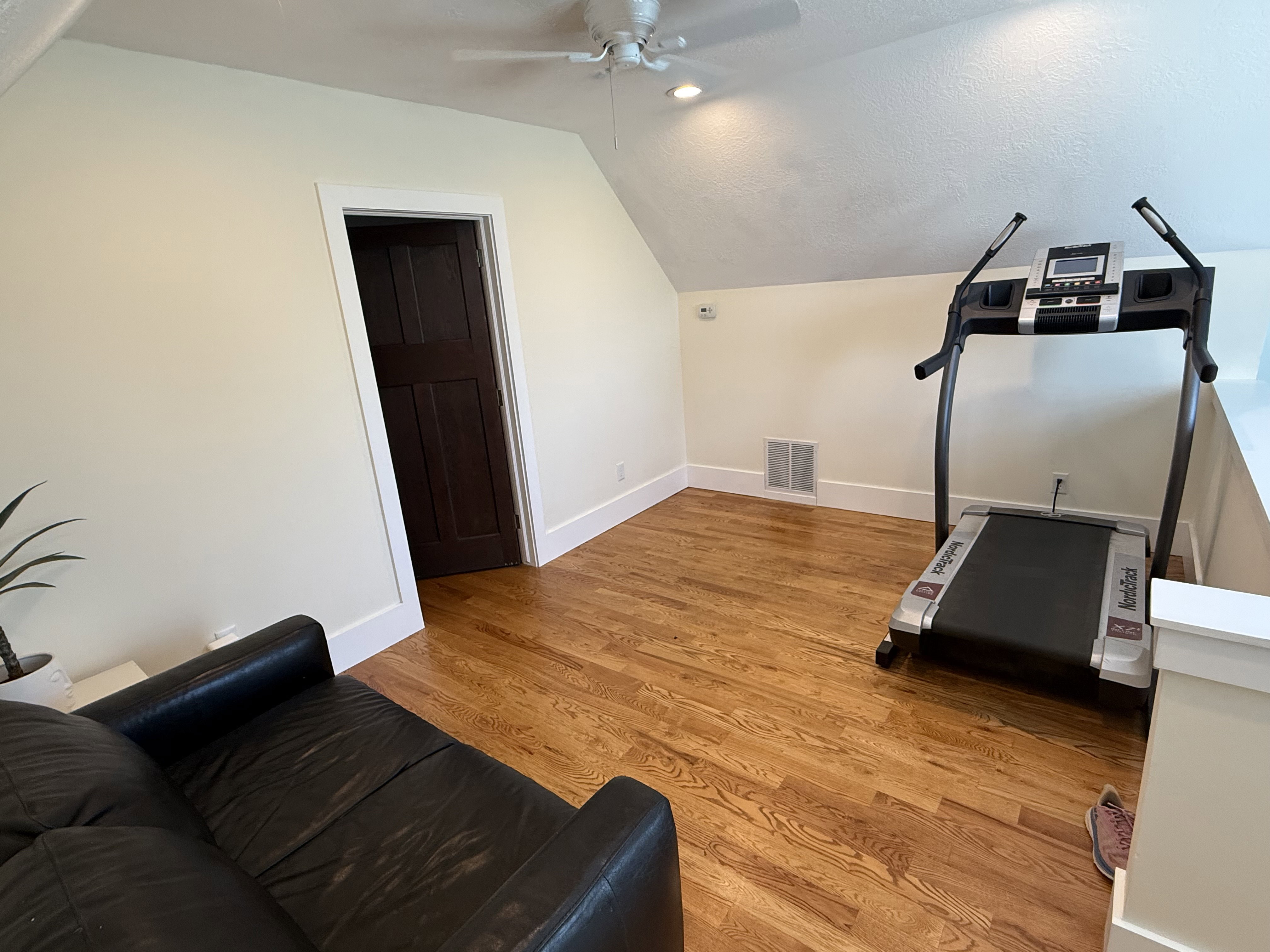 Attic space featuring wood-finish flooring, a ceiling fan with integrated lighting, and a dark wood panel door