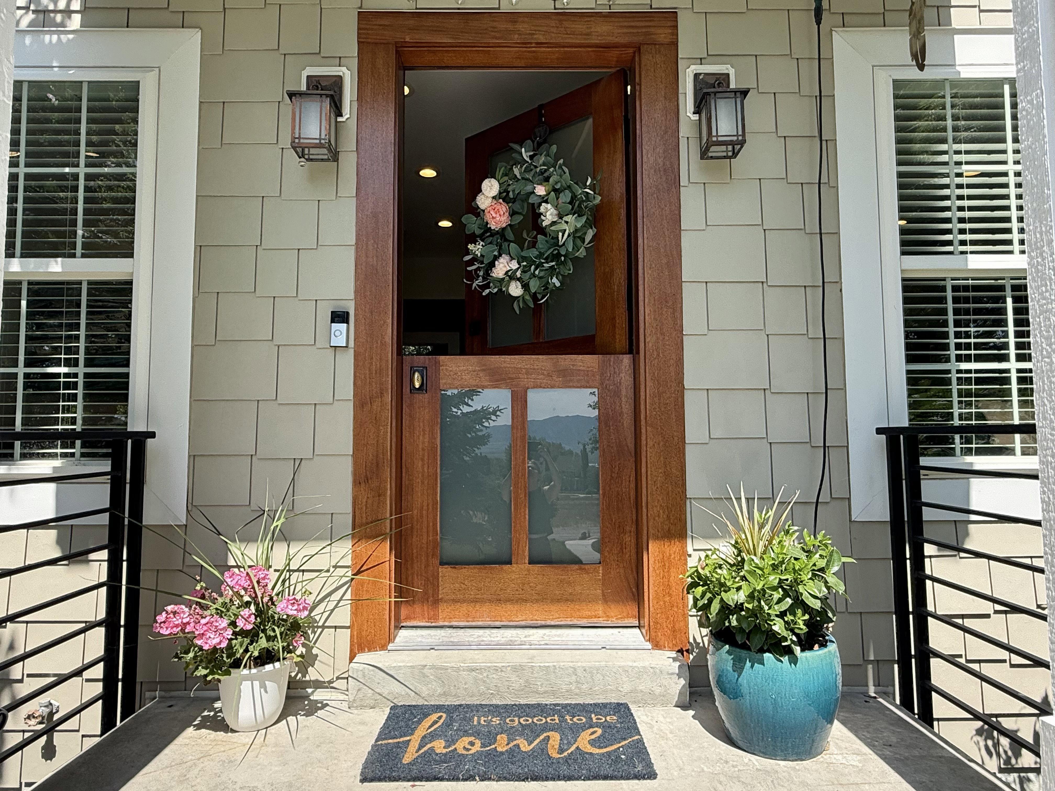 Warm wood-paneled entry door with glass panels, flanked by two bronze-finish exterior sconces
