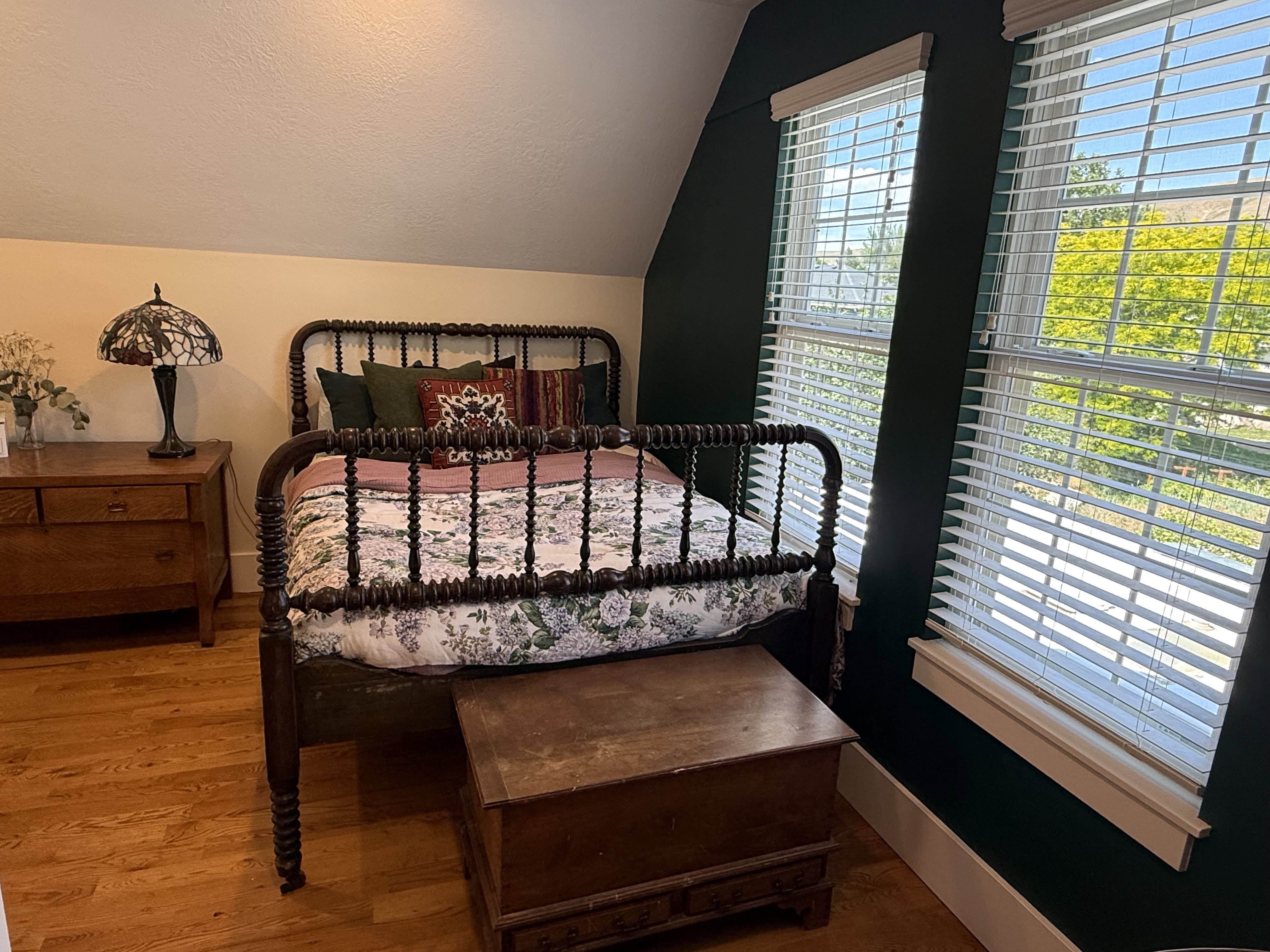 Bright bedroom featuring two windows with horizontal blinds, hardwood flooring, and a unique architectural ceiling line