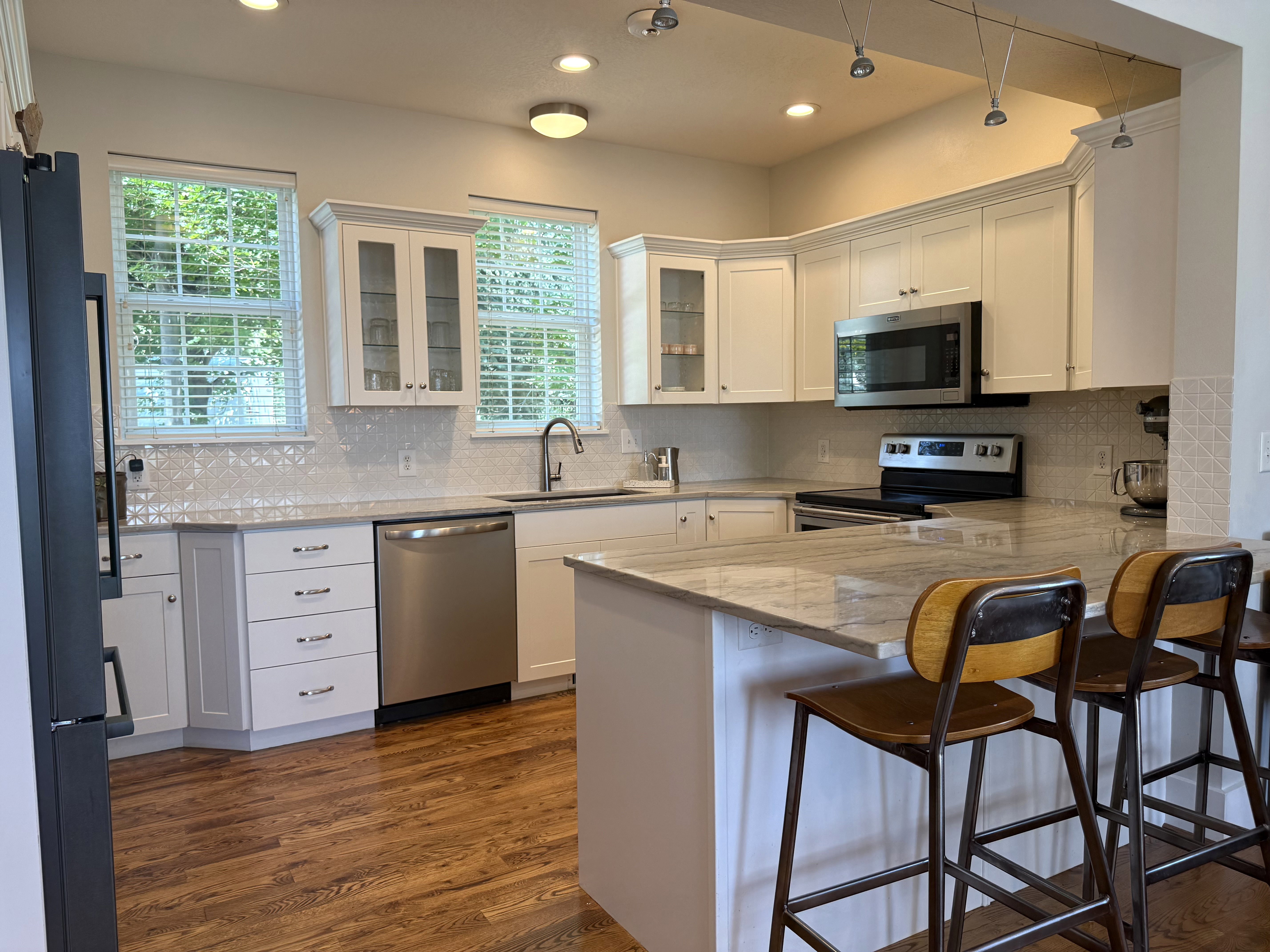 Kitchen featuring a large central island with seating, stainless steel appliances, white shaker cabinetry, patterned tile backsplash, and wood-finish flooring