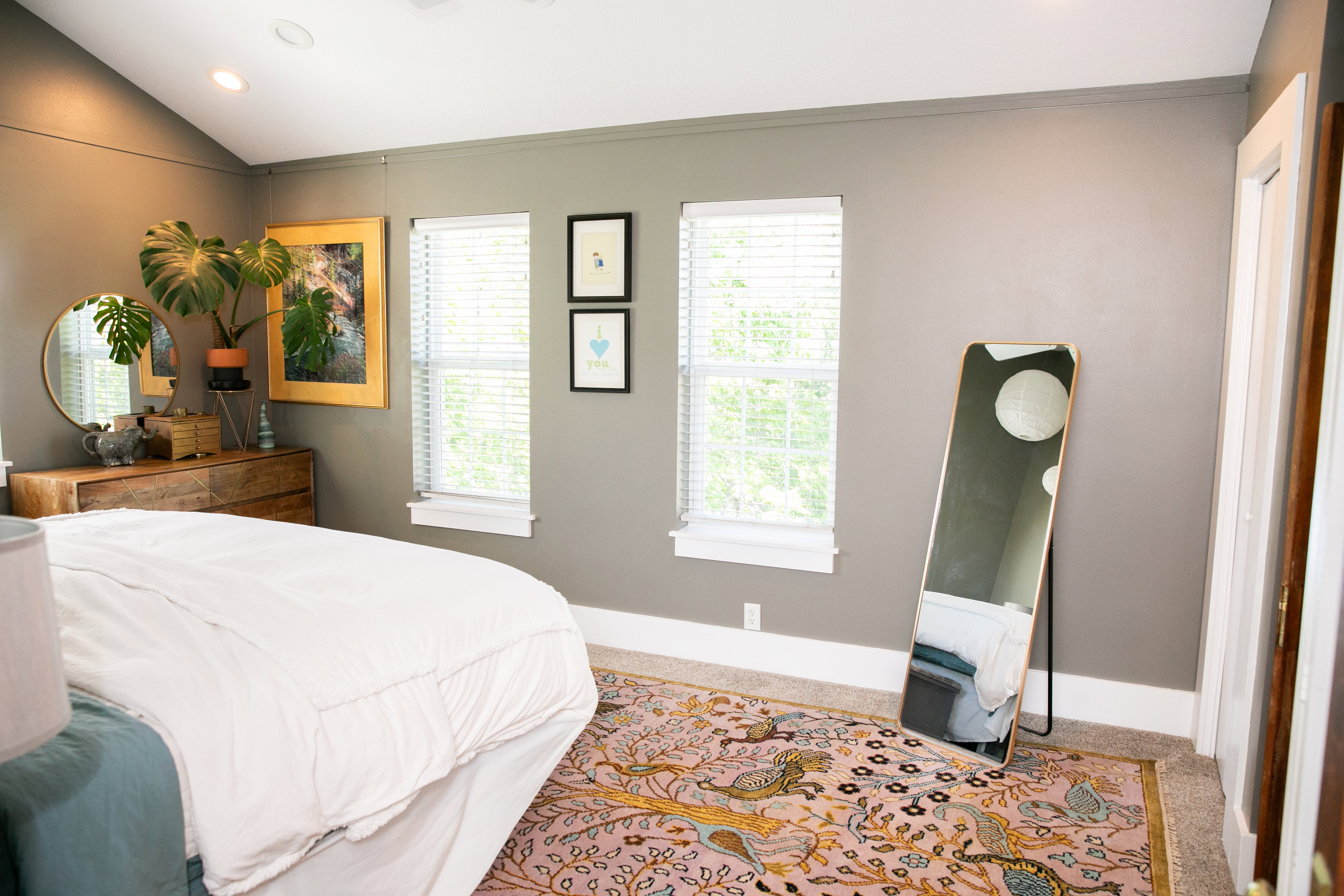 Spacious room featuring vaulted ceilings, recessed lighting, two windows with blinds, a built-in wooden dresser, and a vibrant patterned area rug