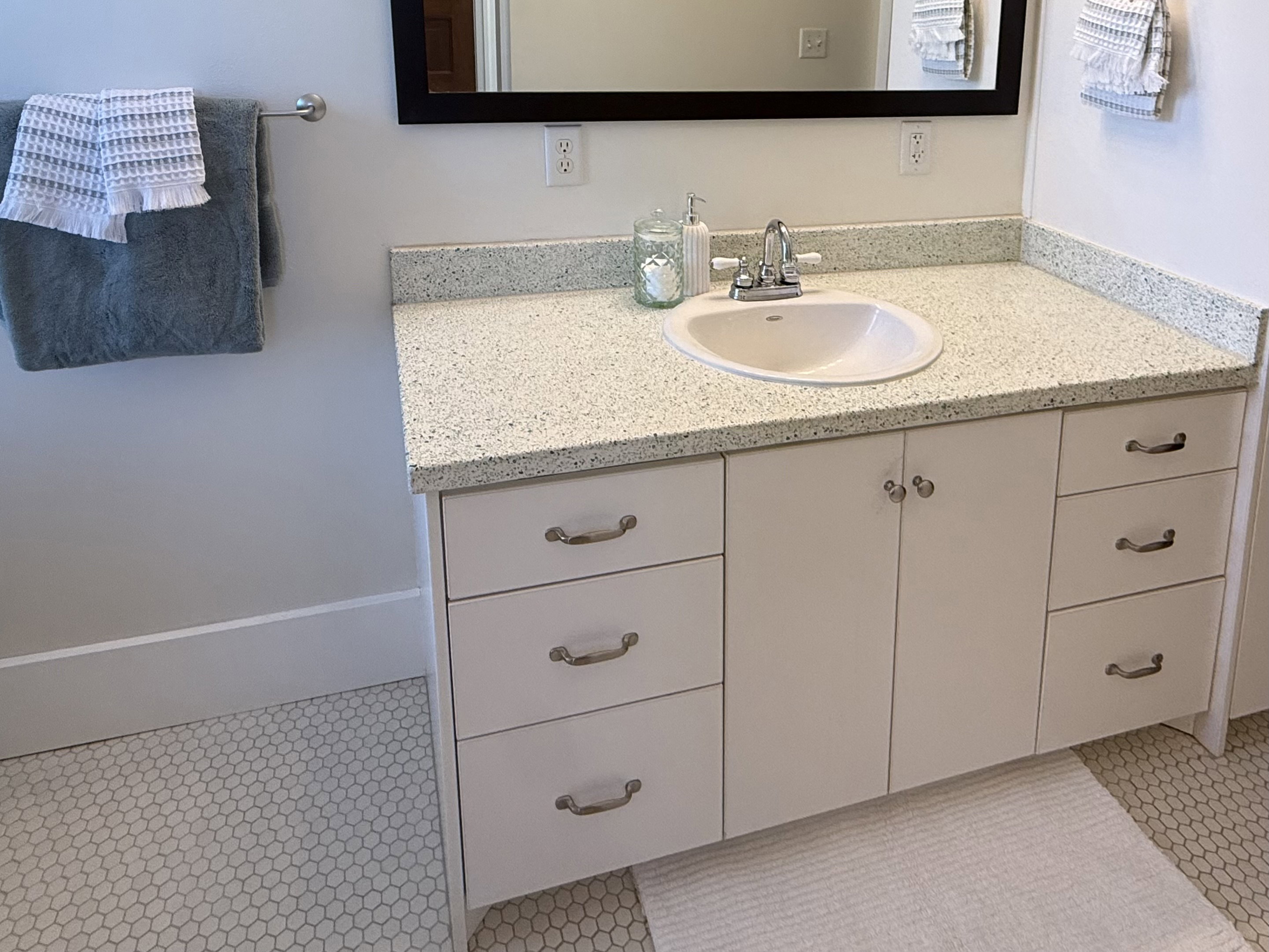 Bathroom vanity featuring a white undermount sink, speckled countertop, and white cabinetry with brushed nickel hardware