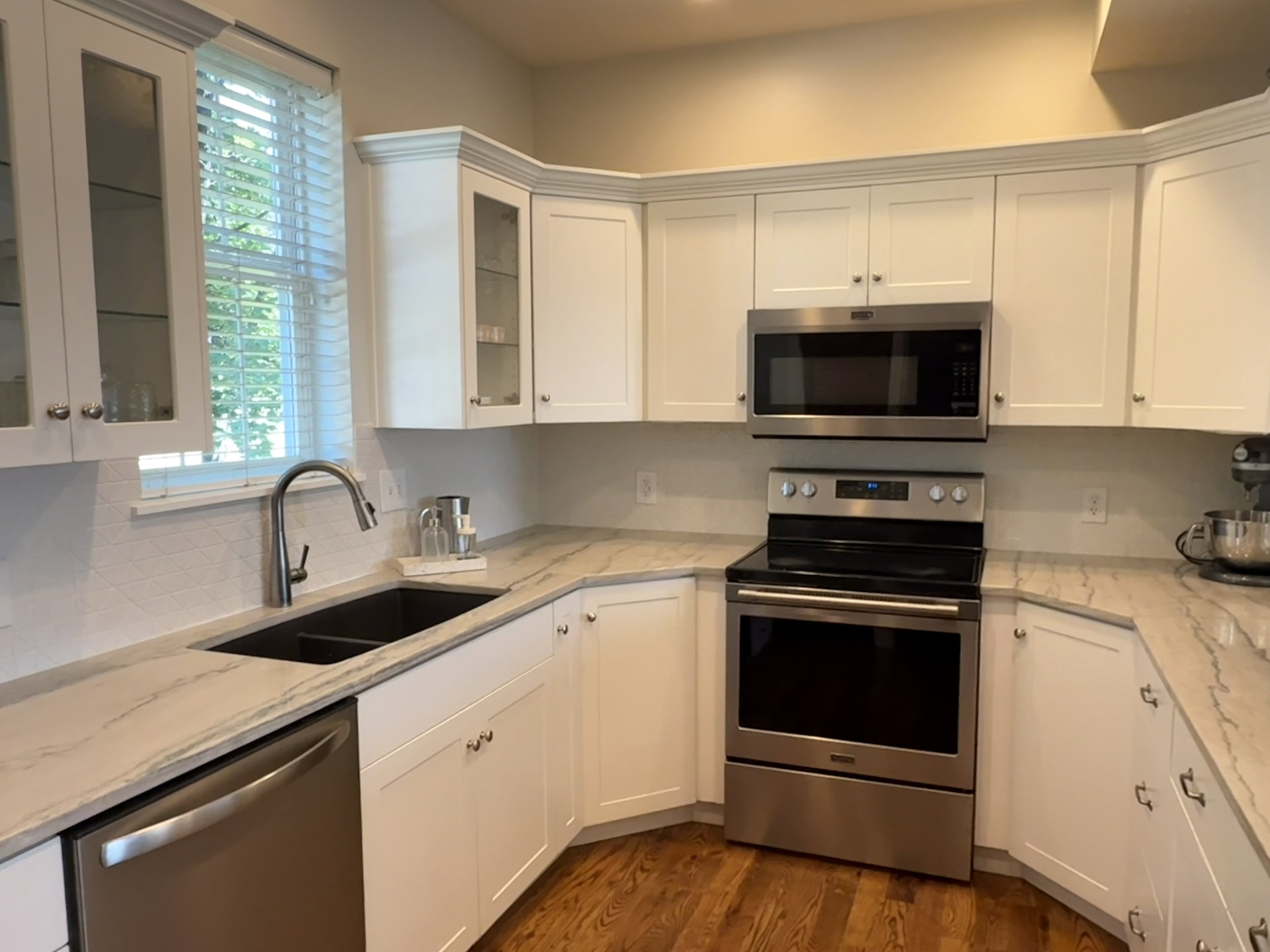 Kitchen featuring white cabinetry, stainless steel appliances, patterned backsplash, undermount sink, and wood-finish flooring