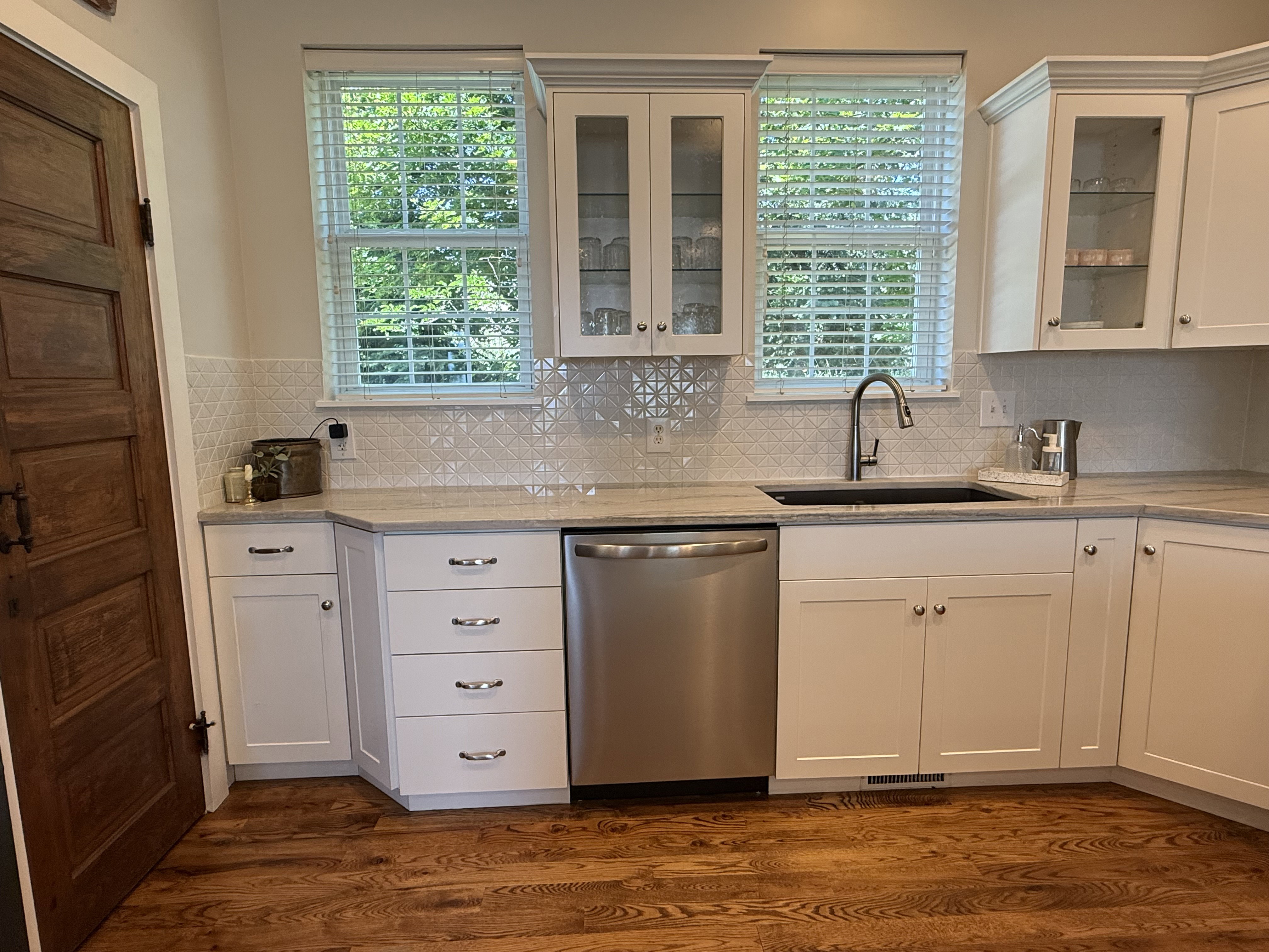 Kitchen featuring wood-finish flooring, white cabinetry, integrated stainless steel dishwasher, undermount sink with a gooseneck faucet, and light-toned countertops