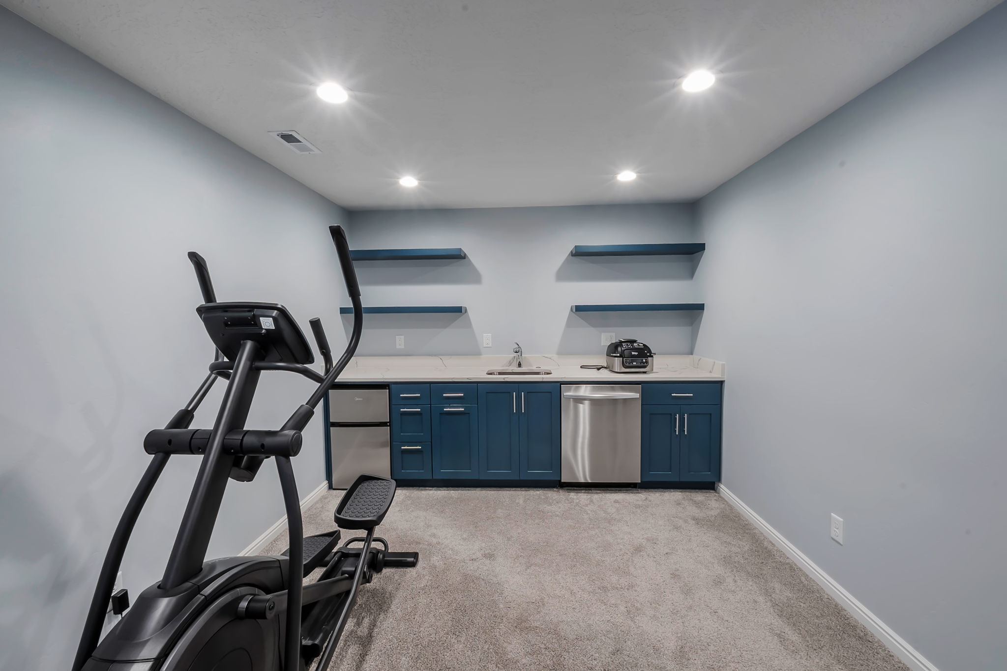 Dedicated flex space featuring a wet bar with dark blue cabinetry, a stainless steel sink, and a built-in dishwasher