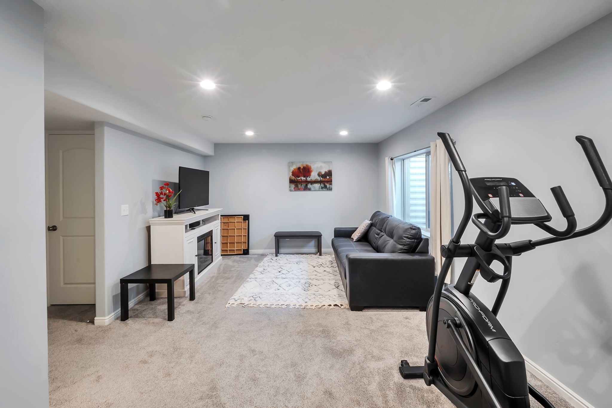 Spacious carpeted room featuring recessed lighting, a built-in electric fireplace unit, a white paneled door, and a horizontal window with blinds