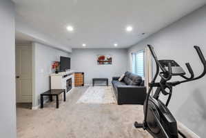 Spacious carpeted room featuring recessed lighting, a built-in electric fireplace unit, a white paneled door, and a horizontal window with blinds