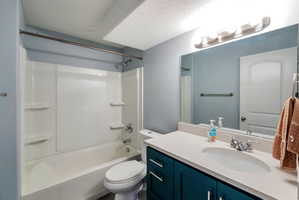 Full bathroom featuring a single vanity with integrated sink, stone-finish countertop, and teal cabinetry