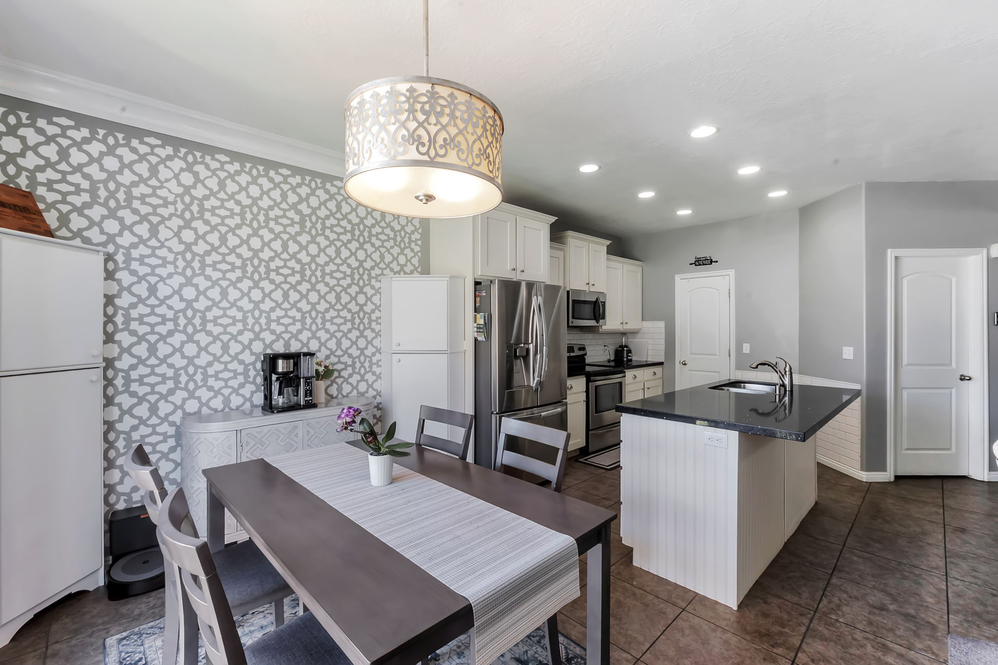 Open-concept kitchen and dining area featuring a decorative accent wall and an ornate drum pendant light