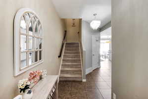 Foyer featuring ceramic tile flooring, carpeted staircase with wood handrail, and a contemporary multi-tiered chandelier