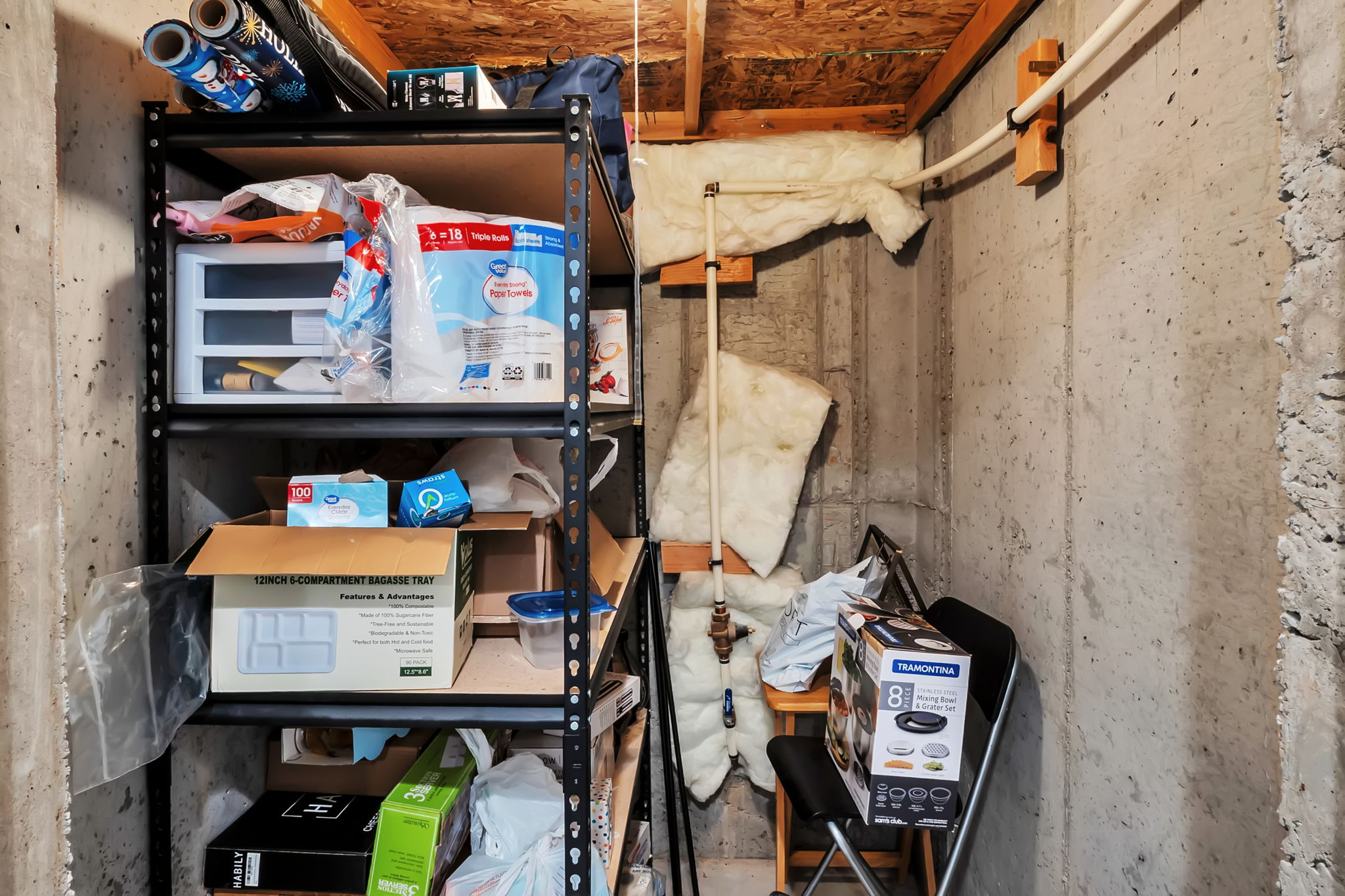 Unfinished basement area featuring exposed concrete walls, visible wood ceiling joists, and overhead piping