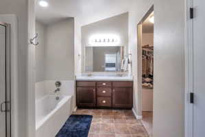 Bathroom featuring a dual vanity with a dark wood-finish cabinet and stone-look countertop, a bathtub with tile surround, and an adjacent walk-in shower with a glass enclosure