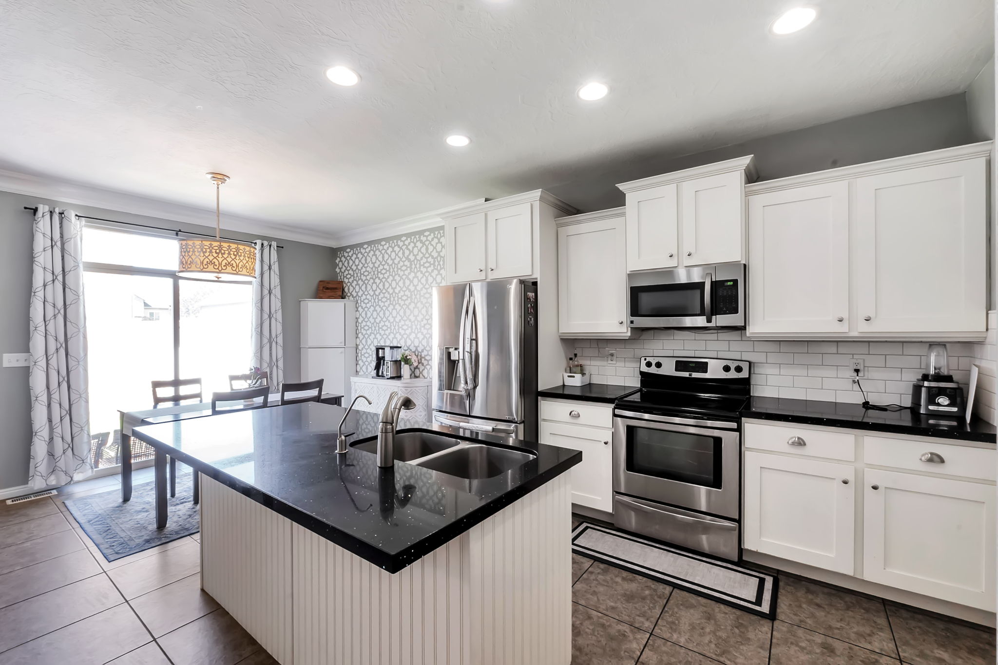 Kitchen featuring a large island with an undermount double sink, white cabinetry, black countertops, stainless steel appliances, and subway tile backsplash