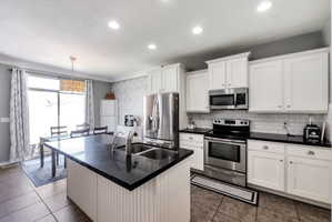 Kitchen featuring a large island with an undermount double sink, white cabinetry, black countertops, stainless steel appliances, and subway tile backsplash