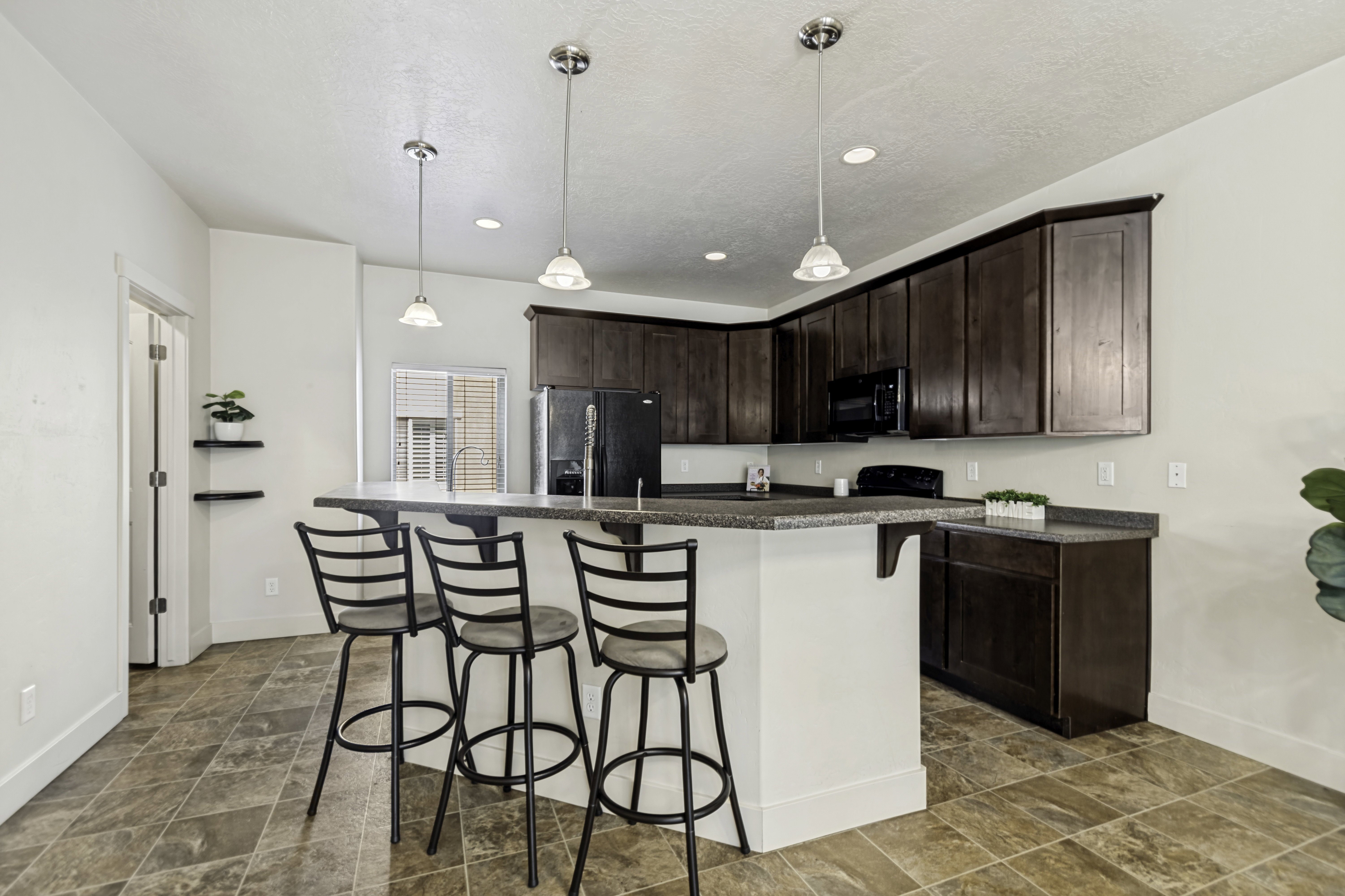 Kitchen featuring rich wood-finish cabinetry, a large peninsula with seating, speckled countertops, and an integrated black appliance package