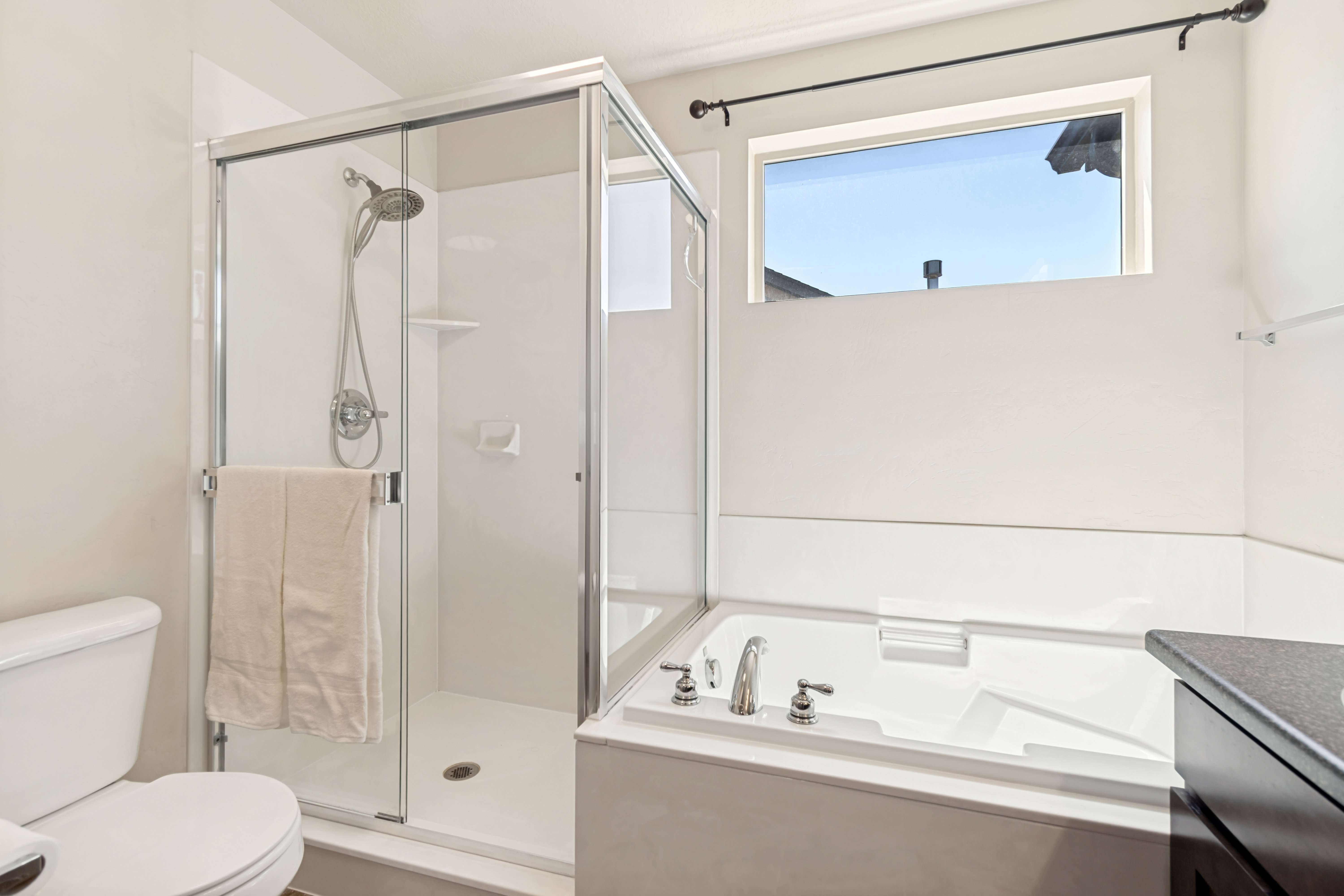 Bathroom featuring a glass-enclosed shower, a built-in soaking tub with chrome fixtures, a privacy window, and a dark-finished vanity with a stone-finish countertop