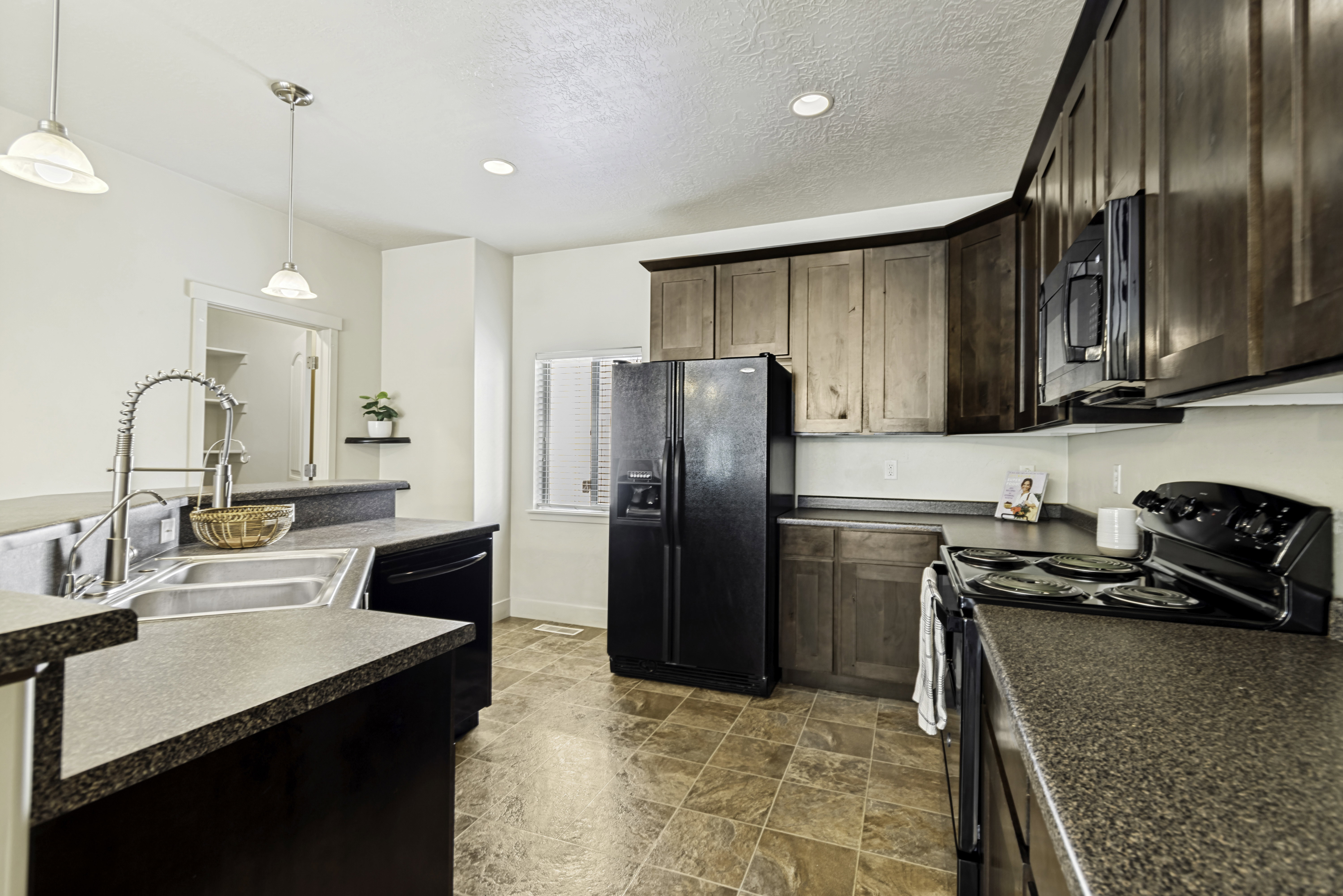 Kitchen featuring dark wood-finish cabinetry, black appliances, a double basin stainless steel sink with a high-arc faucet, and mottled gray countertops