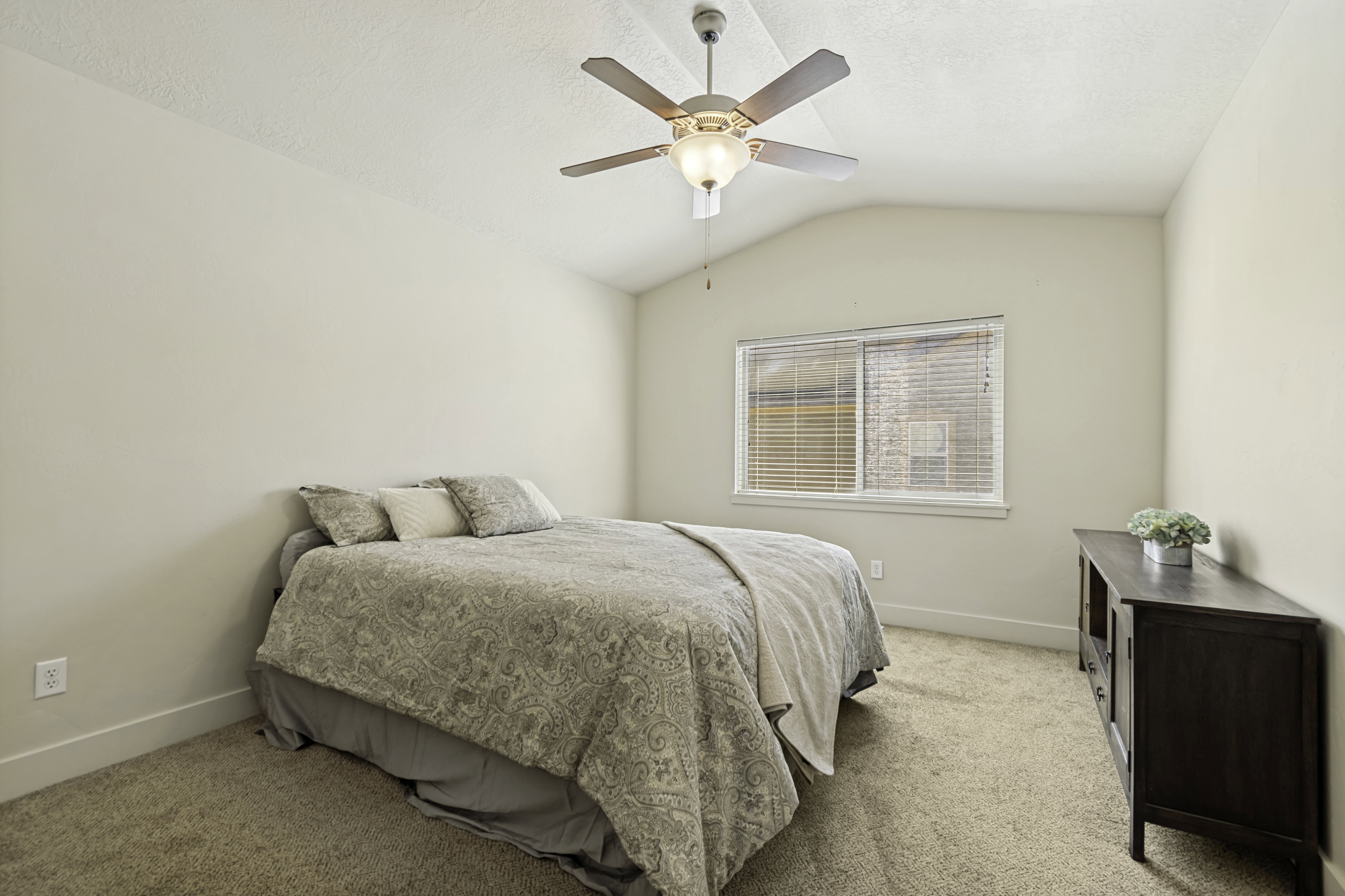 Vaulted ceiling bedroom with a ceiling fan, light-toned carpeting, and a window featuring horizontal blinds