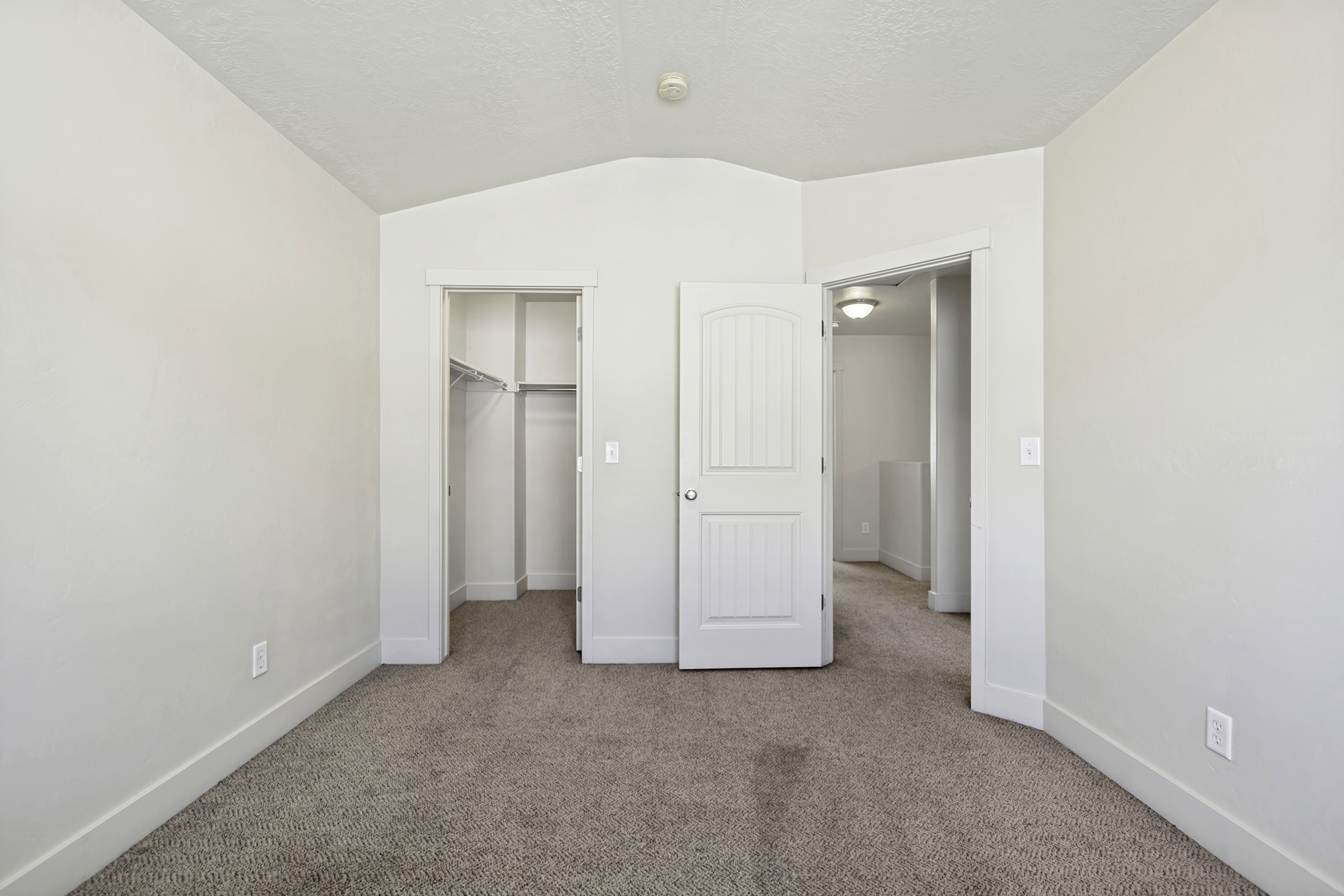 Carpeted room featuring a vaulted ceiling, a closet with wire shelving, and a white paneled door