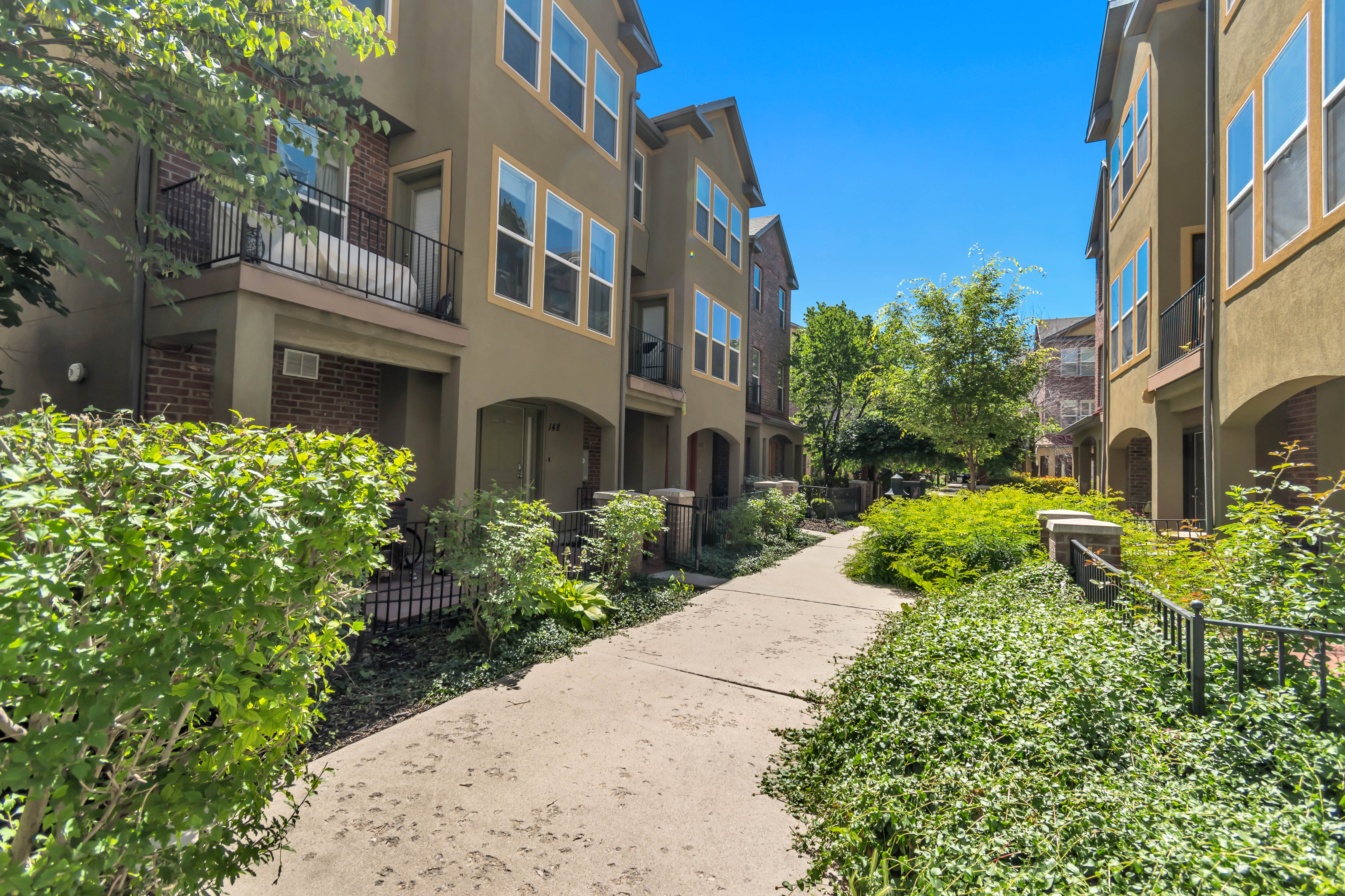 Multi-level townhome featuring a stucco exterior with brick accents, arched entryways, and upper-level balconies with black metal railings
