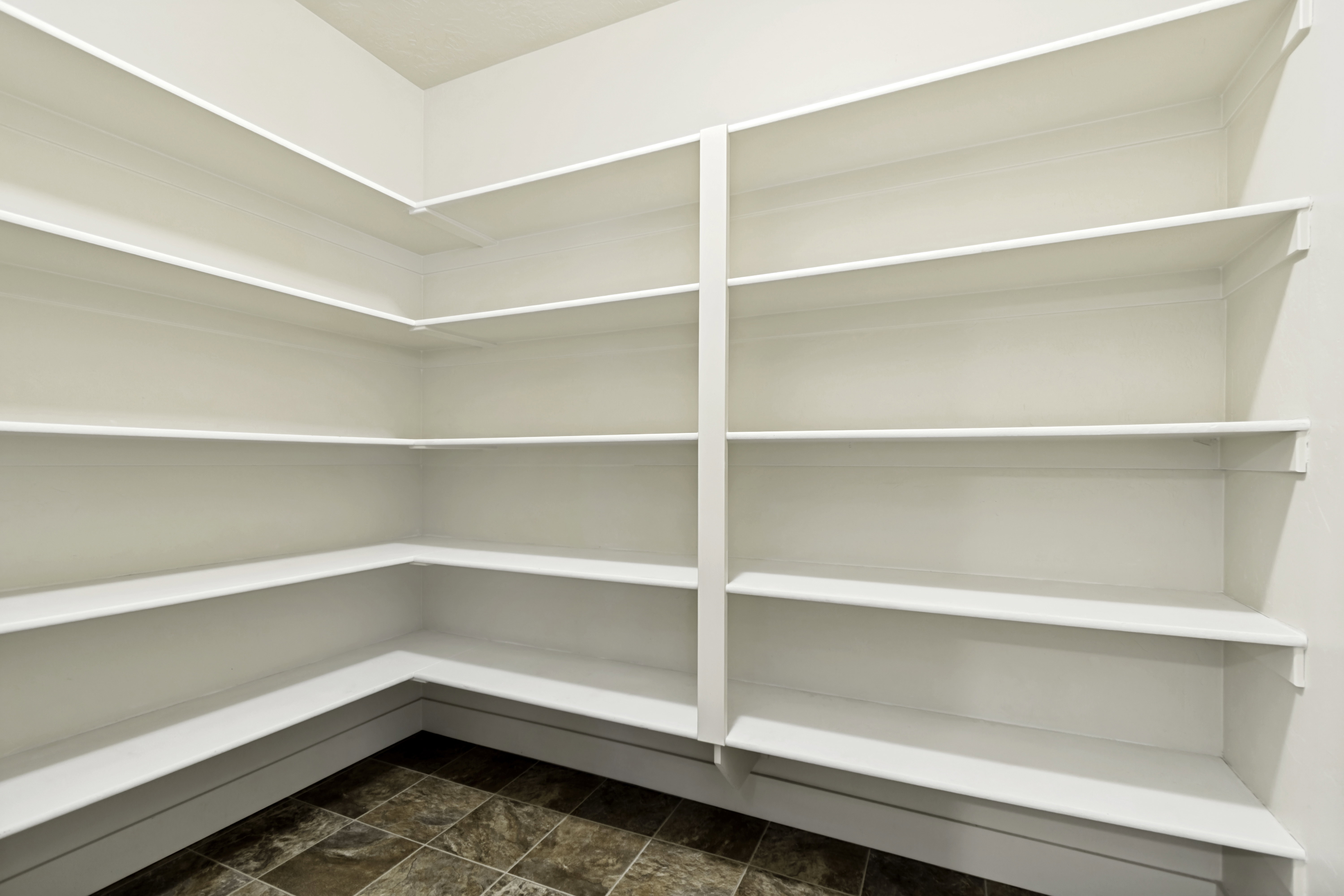 Expansive pantry featuring multi-level built-in shelving, white painted finishes, and durable tile flooring