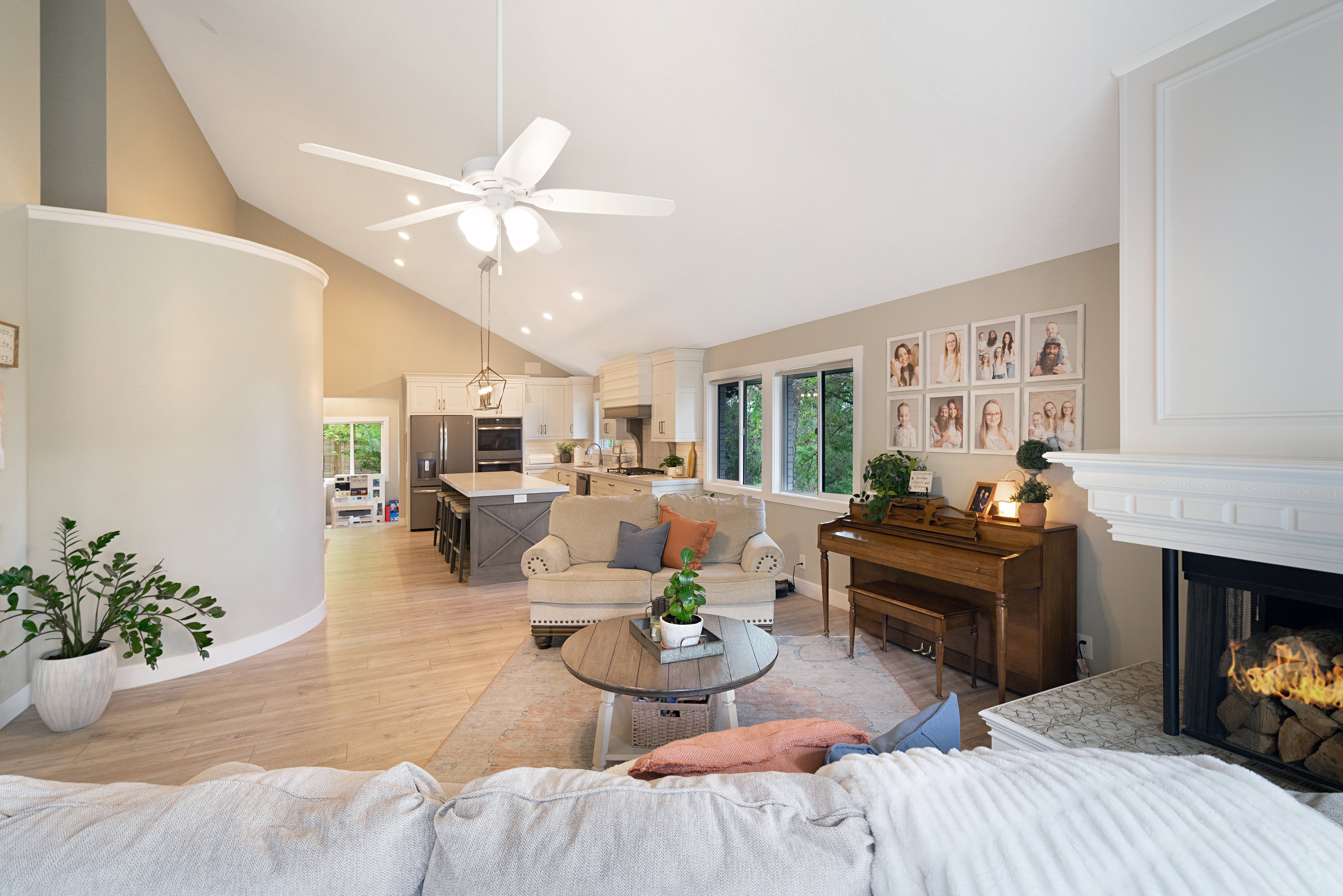 Vaulted ceiling living room featuring a fireplace with a white mantel, wood-finish flooring, recessed lighting, and a ceiling fan