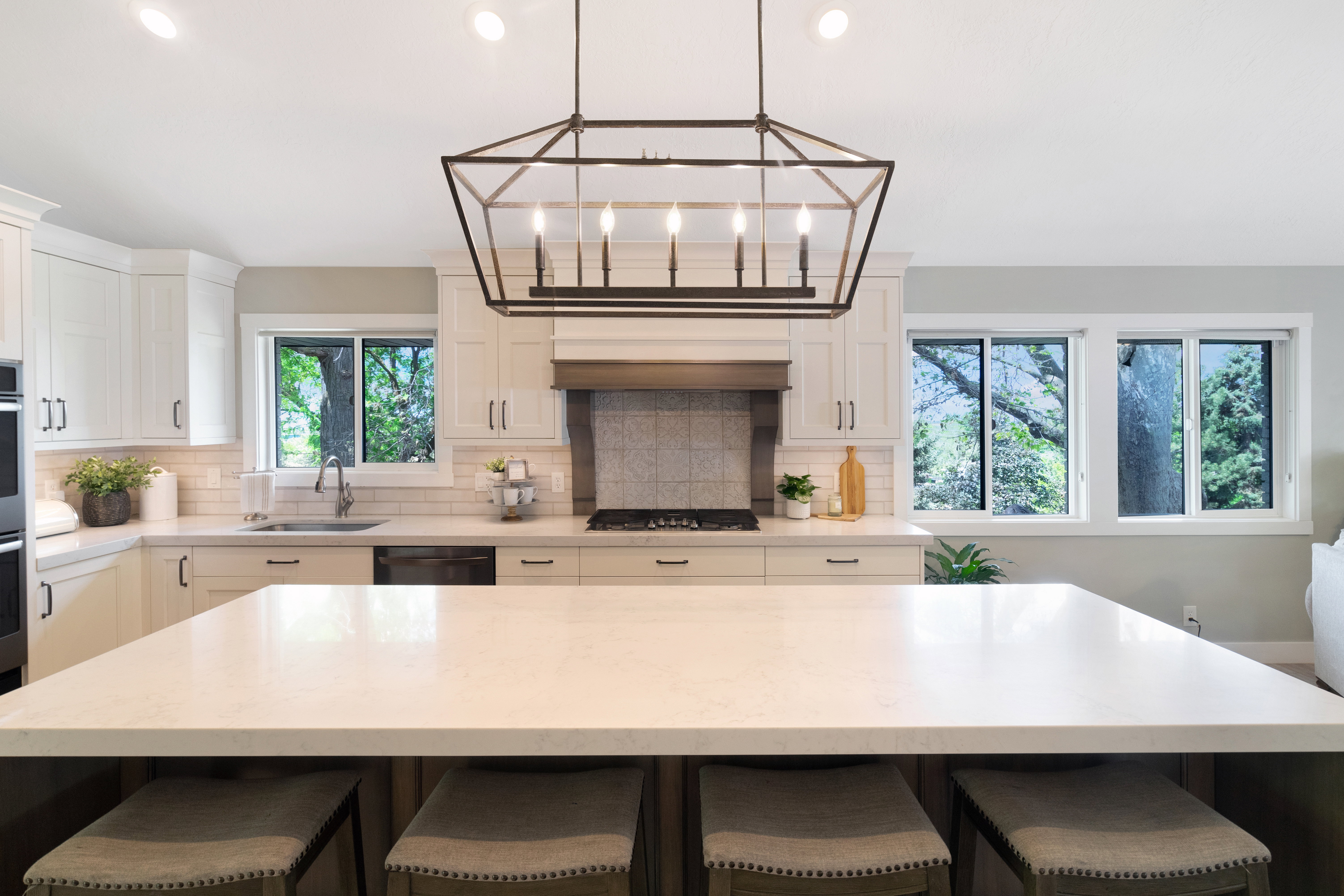 Spacious kitchen with a large central island featuring a light-toned countertop, recessed lighting, and a prominent geometric chandelier