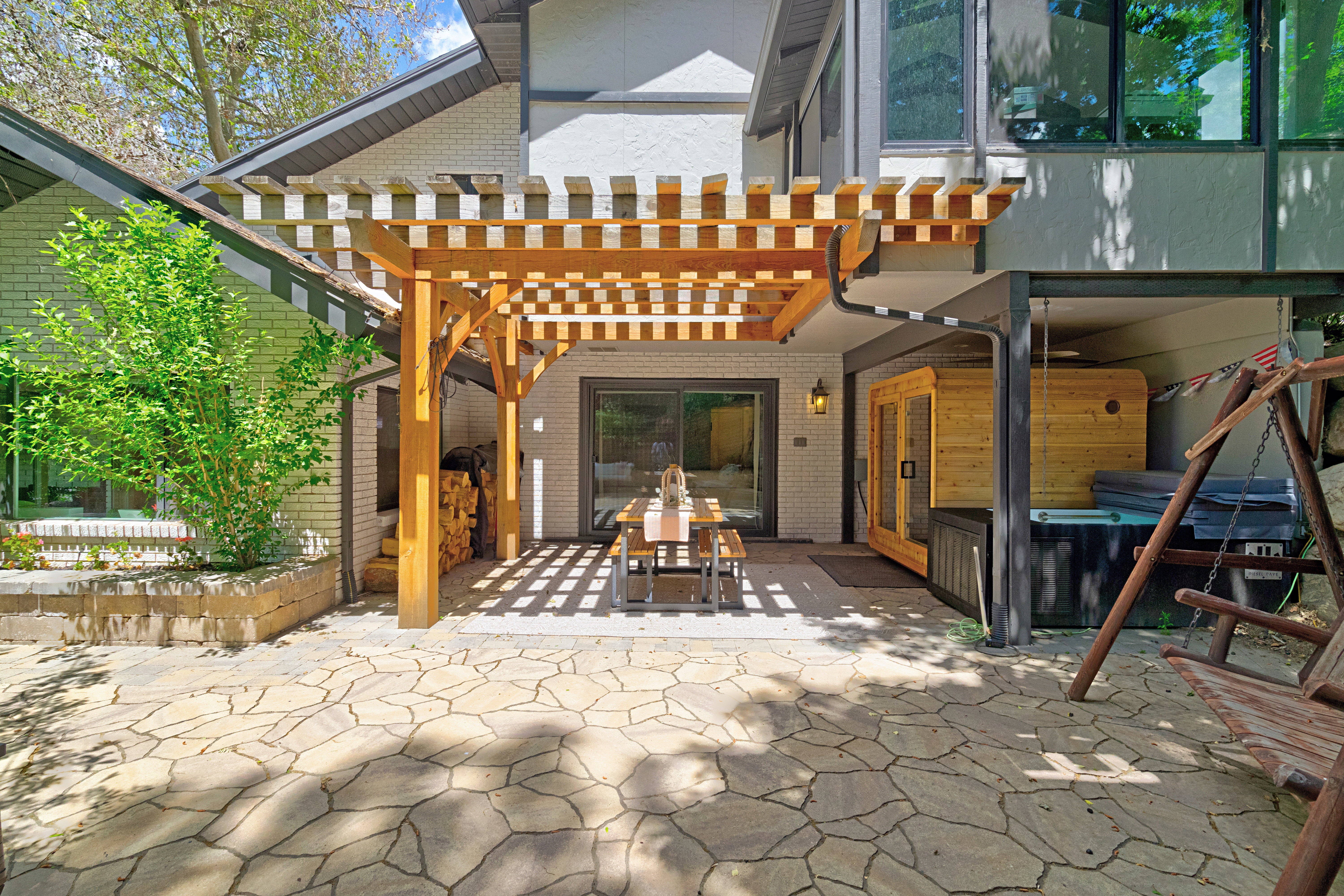 Expansive stone patio featuring a wooden pergola, a built-in outdoor sauna, and a spa area