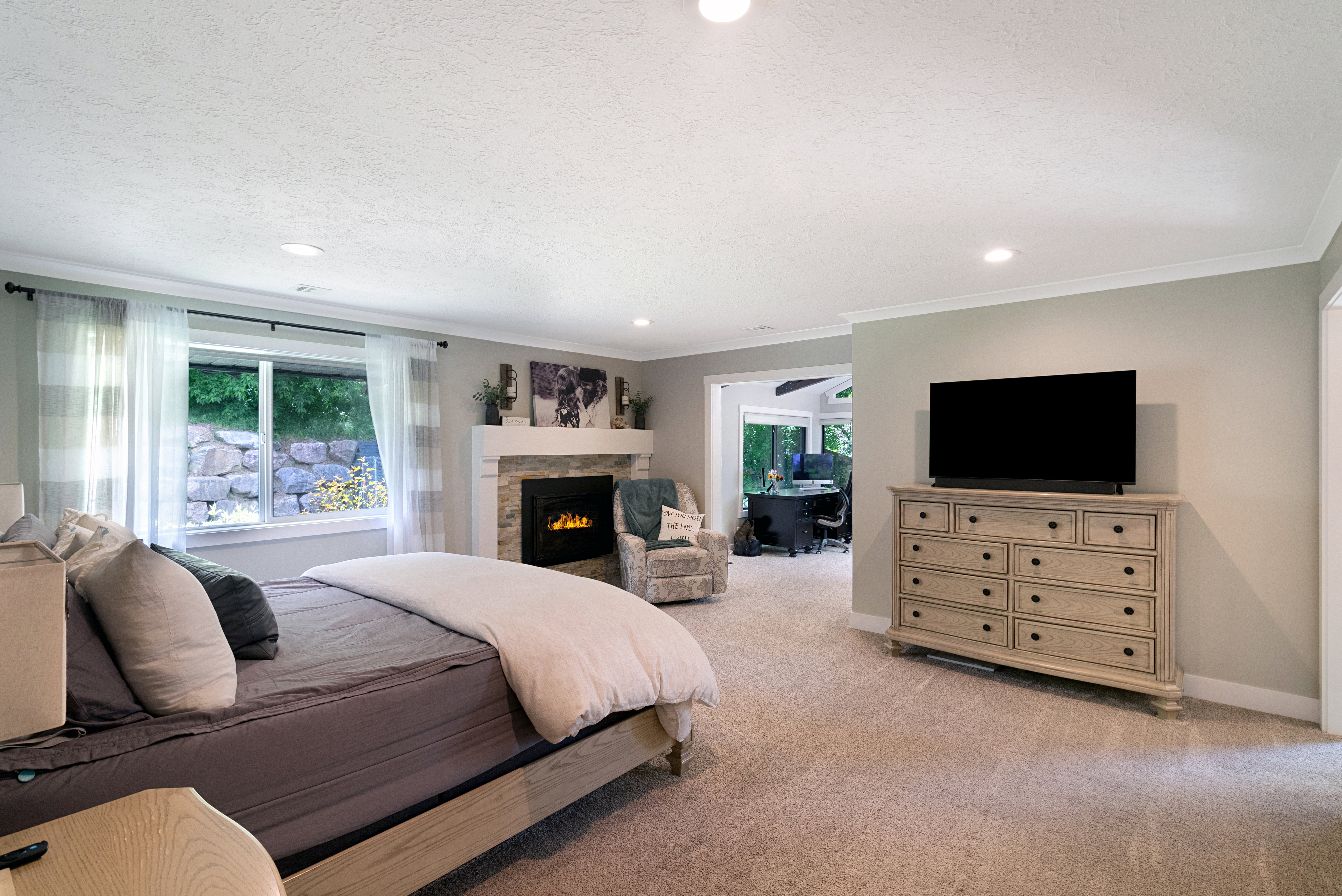 Recessed lighting illuminates this carpeted room featuring a fireplace with a stone surround and substantial mantel