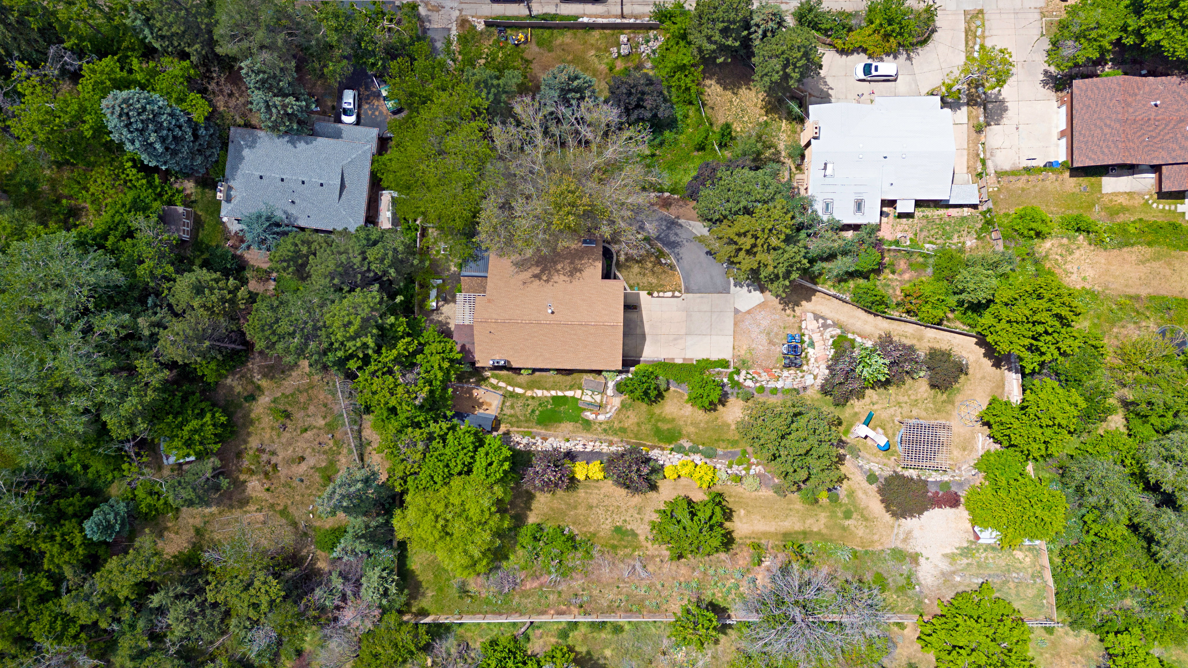 Aerial property perspective featuring a brown shingle roof, mature trees, and a terraced landscape