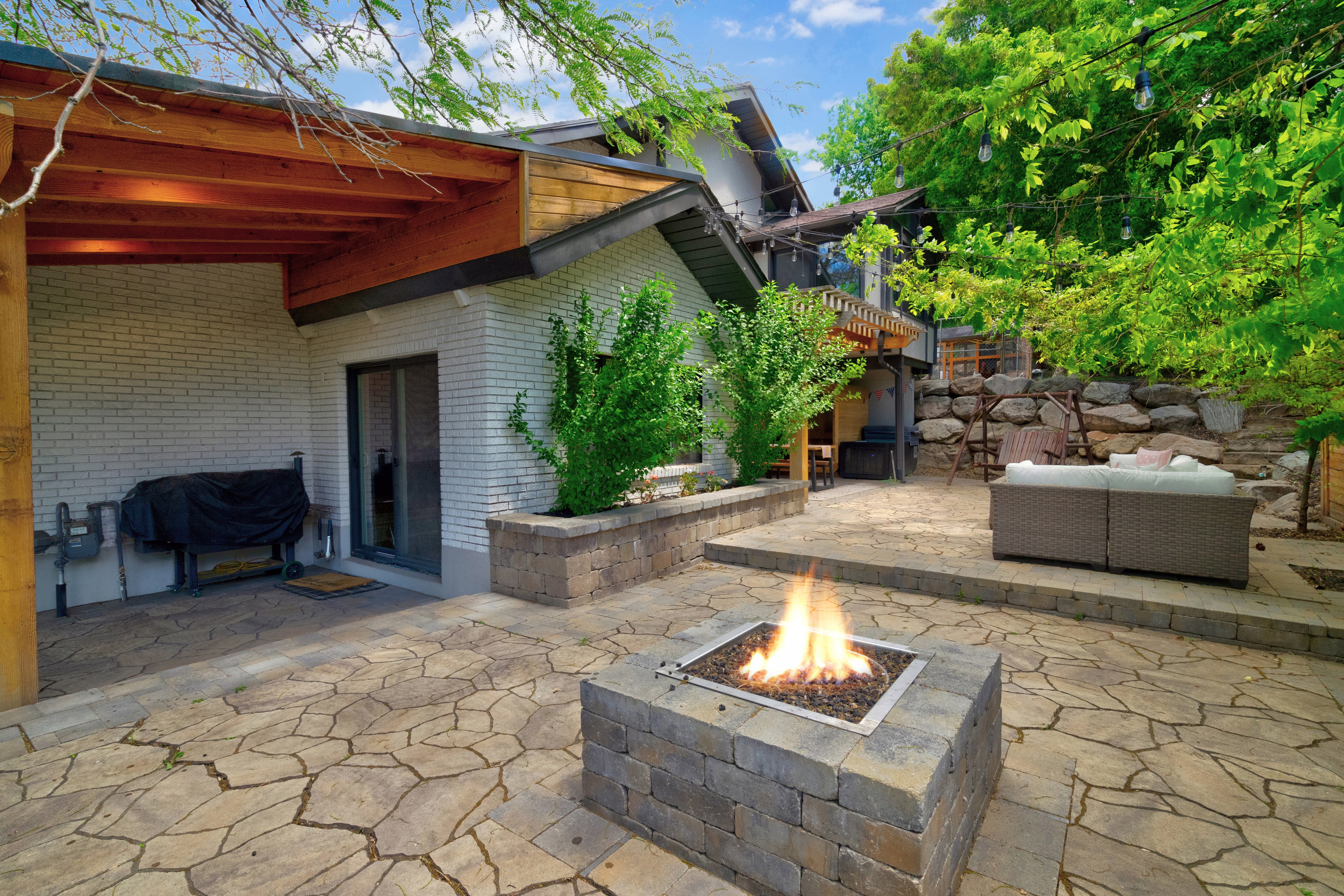 Multi-level flagstone patio featuring a built-in stone fire pit, covered patio space with exposed wood beams, and an upper terrace