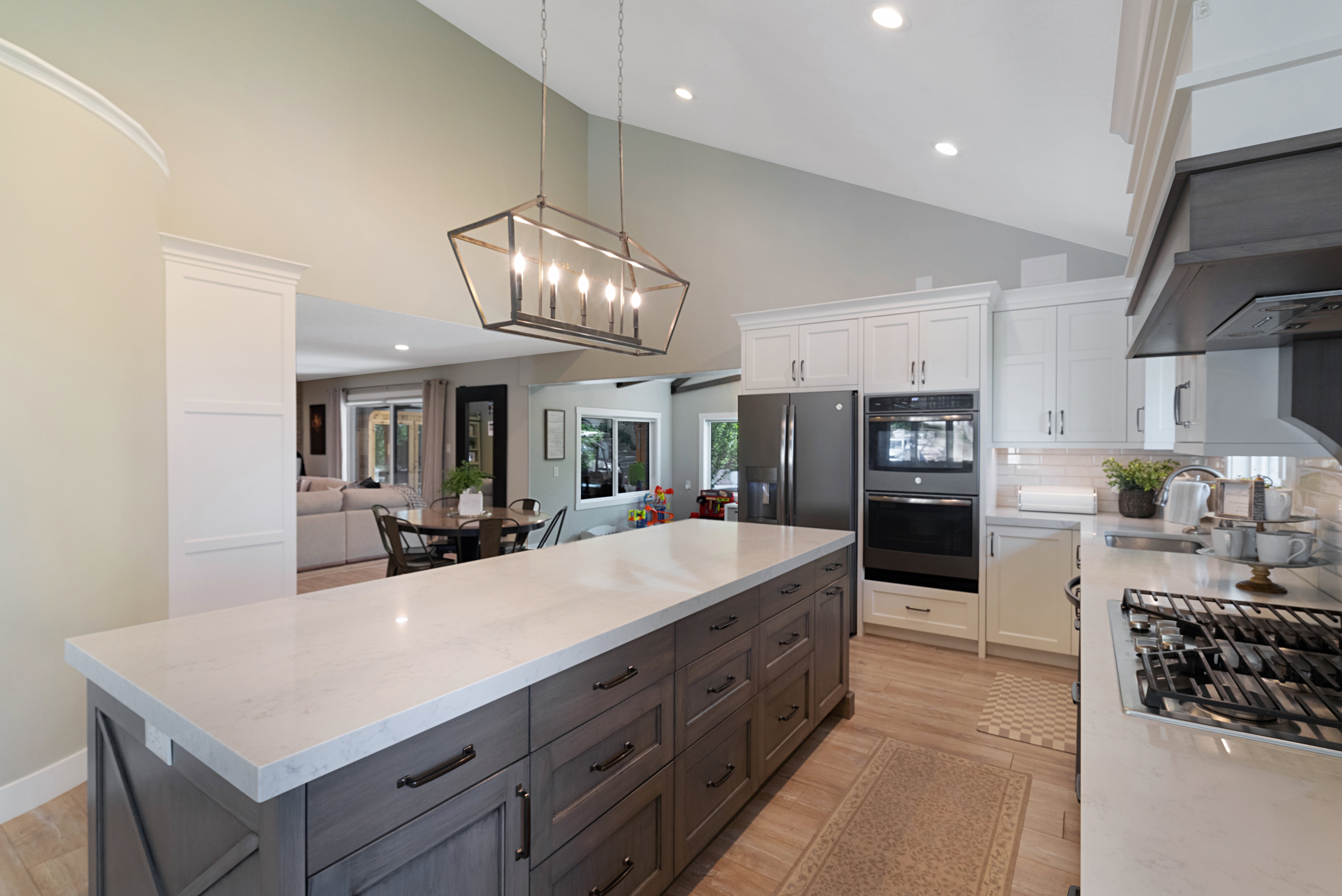 Spacious kitchen featuring a large central island with light-toned countertops, contrasting dark wood-finish cabinetry, and a modern geometric chandelier