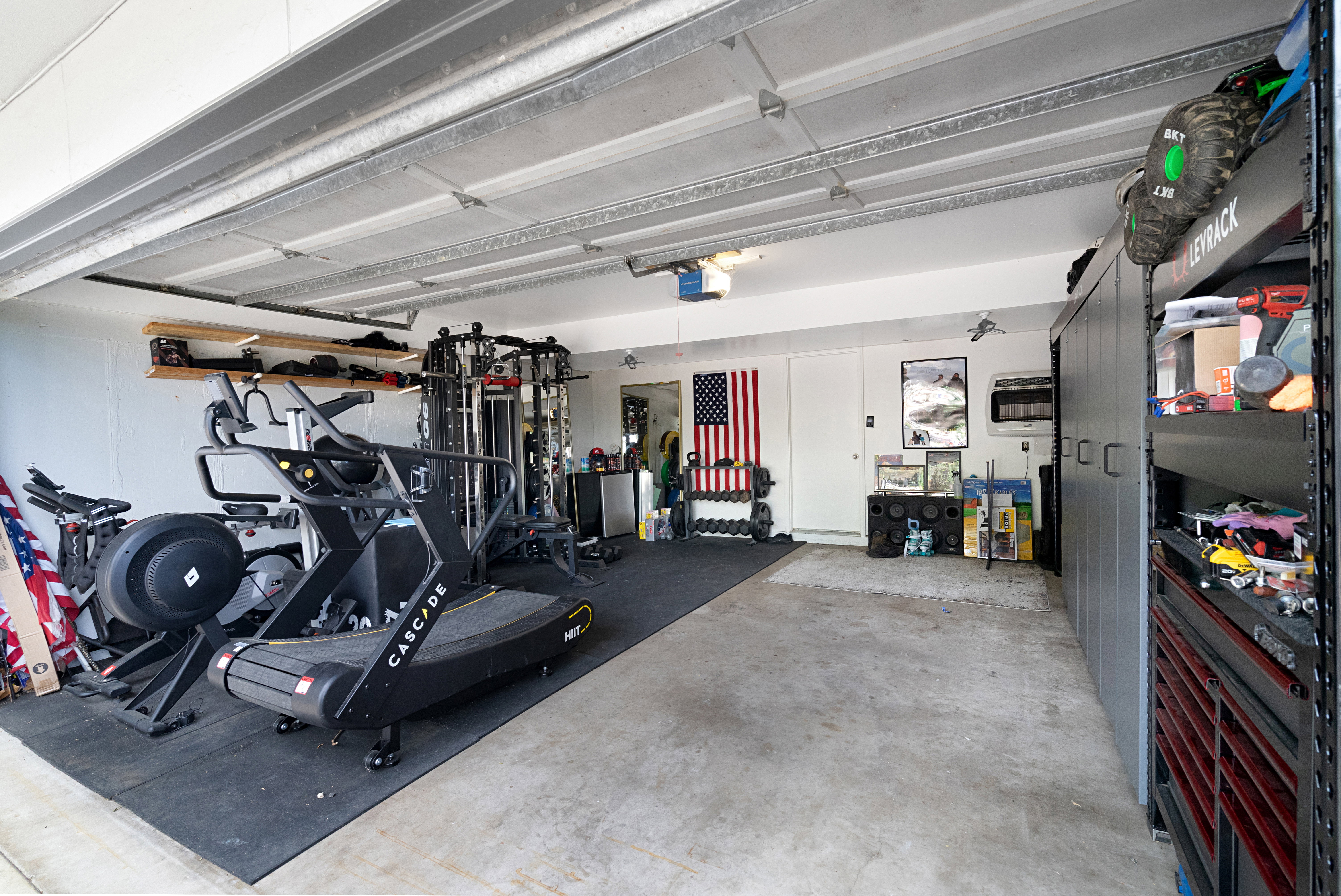 Spacious garage featuring a concrete floor, overhead garage door, built-in shelving, white walls, and dedicated storage cabinetry