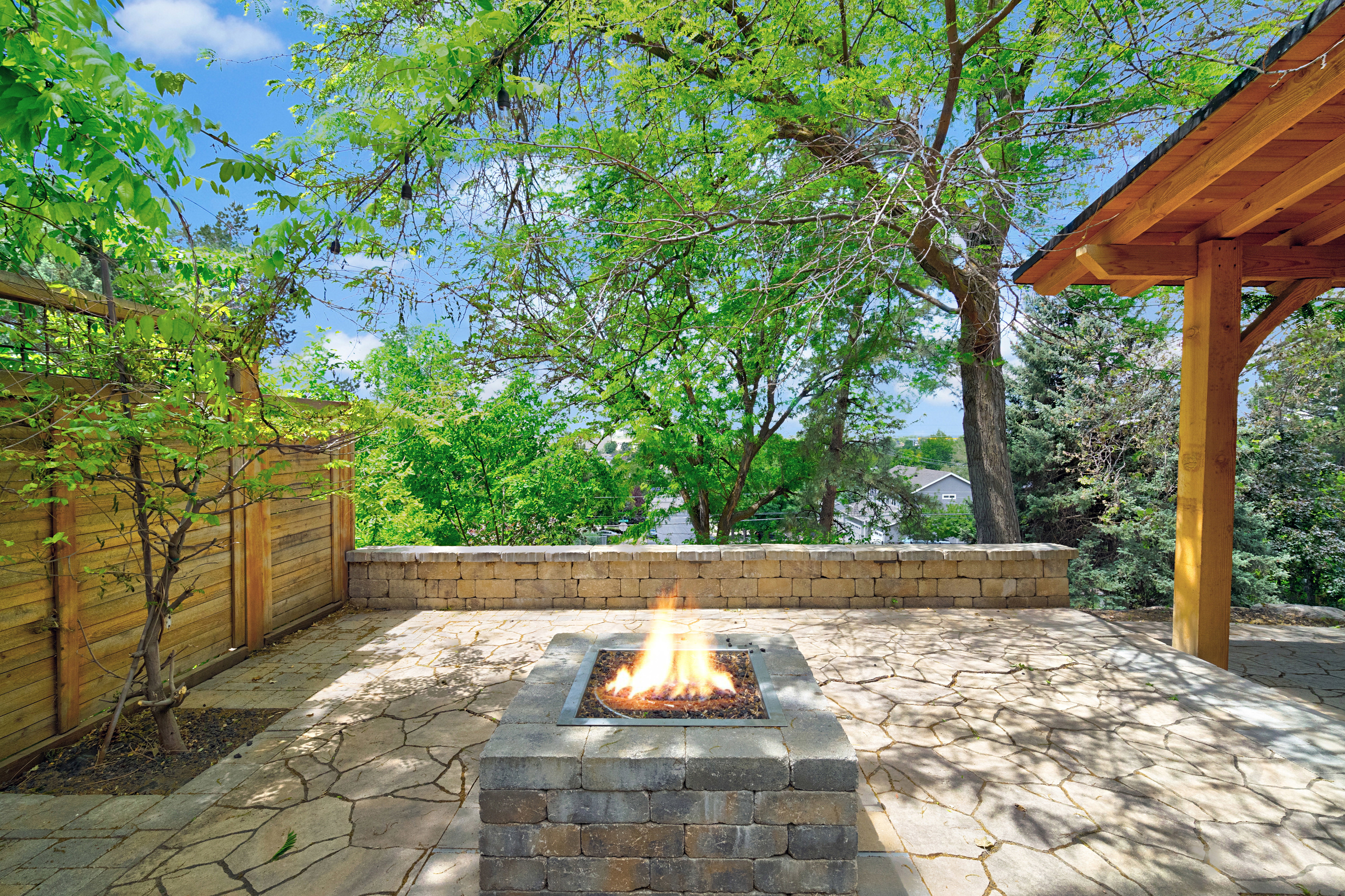 Outdoor patio featuring flagstone paving, a built-in block fire pit, a natural wood privacy fence, and a timber-framed pergola structure