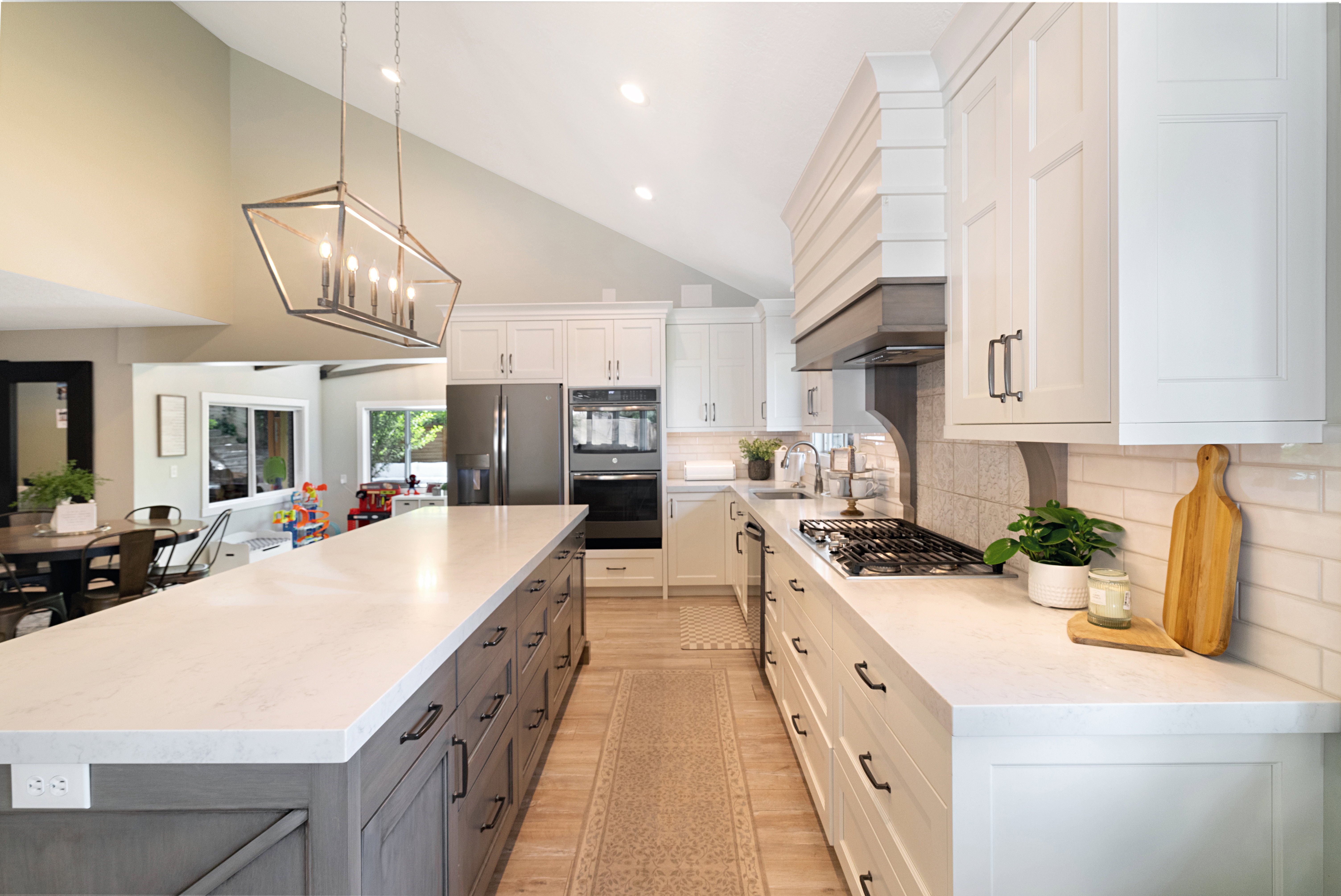 Spacious kitchen featuring a large central island with seating, a gas range with a decorative hood, stainless steel appliances, white subway tile backsplash, and wood-finish flooring