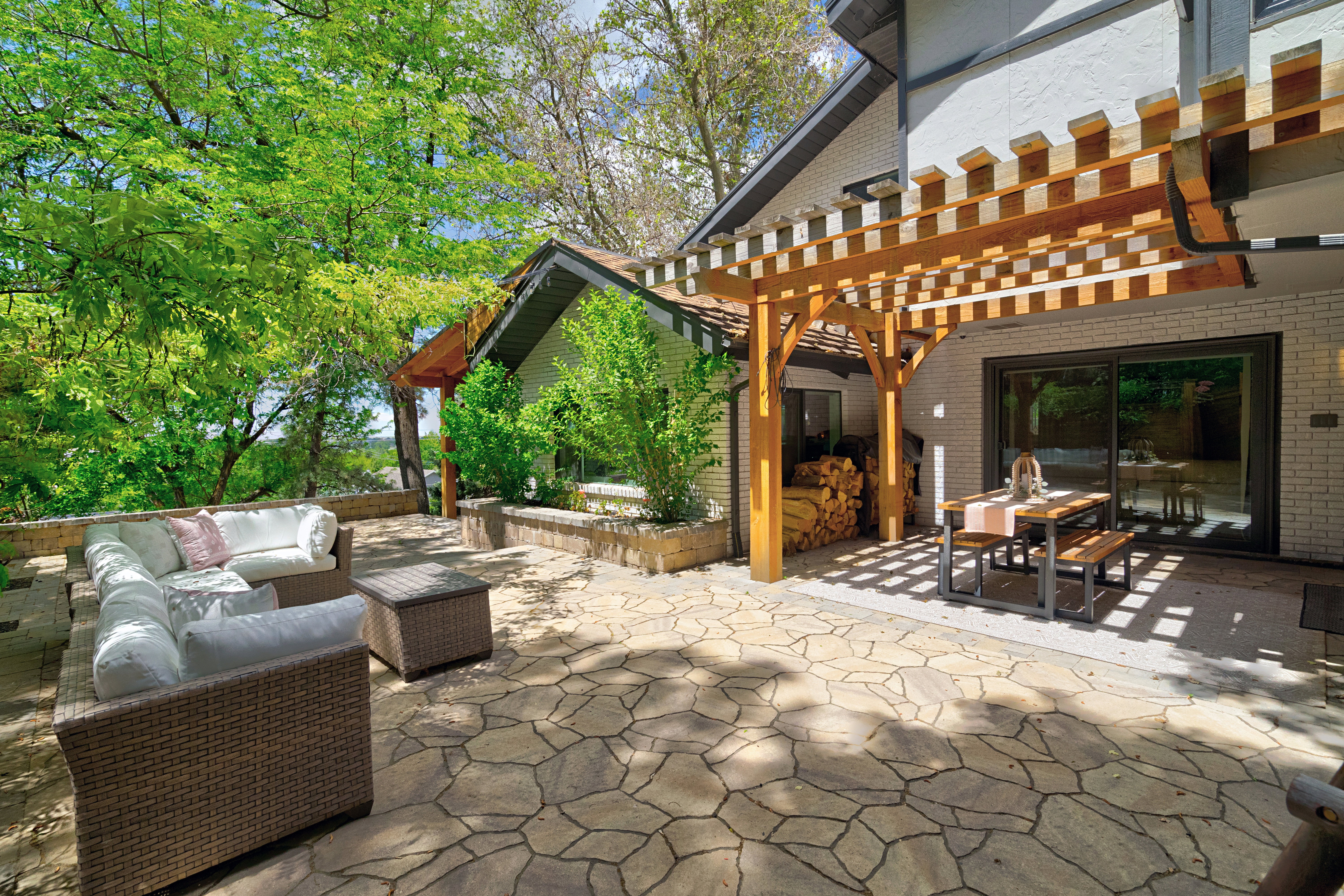 Expansive flagstone patio featuring a wooden pergola and a sliding glass door entry