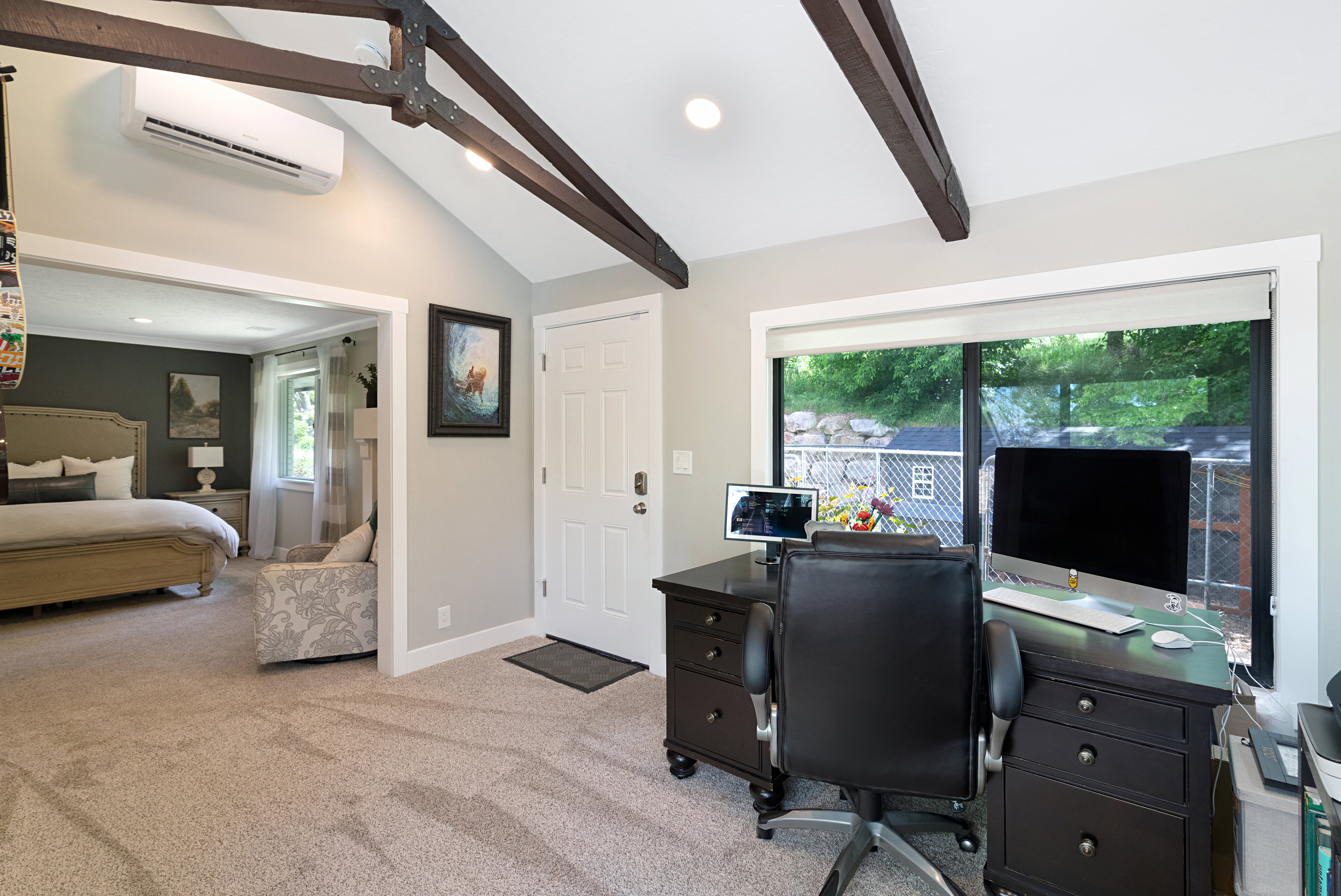 Vaulted ceiling with exposed wood beams, split-system air conditioning unit, large sliding glass door, paneled door, and recessed lighting