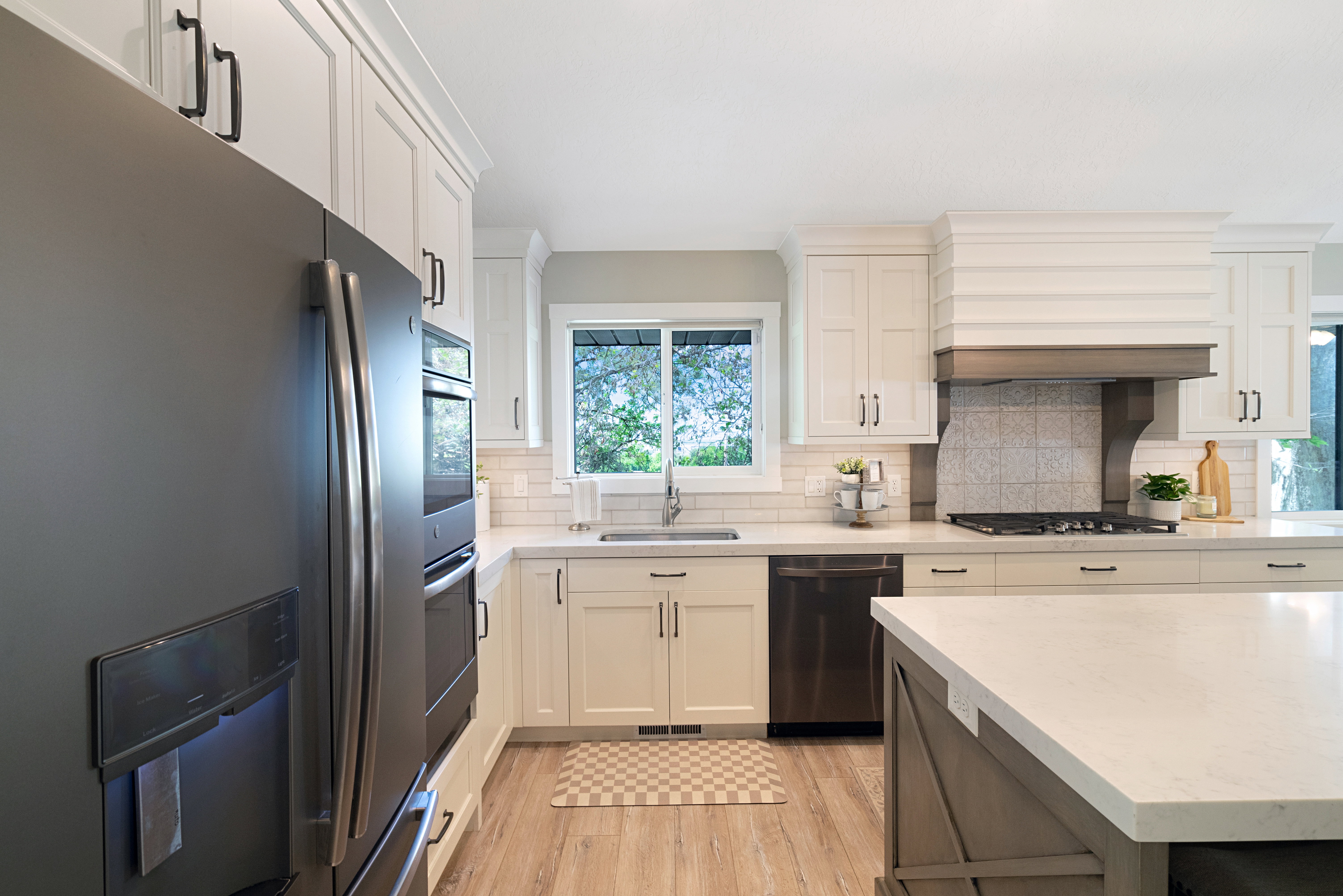 Kitchen featuring white shaker cabinetry, stainless steel appliances, light wood-finish flooring, a built-in kitchen island, and a tile backsplash